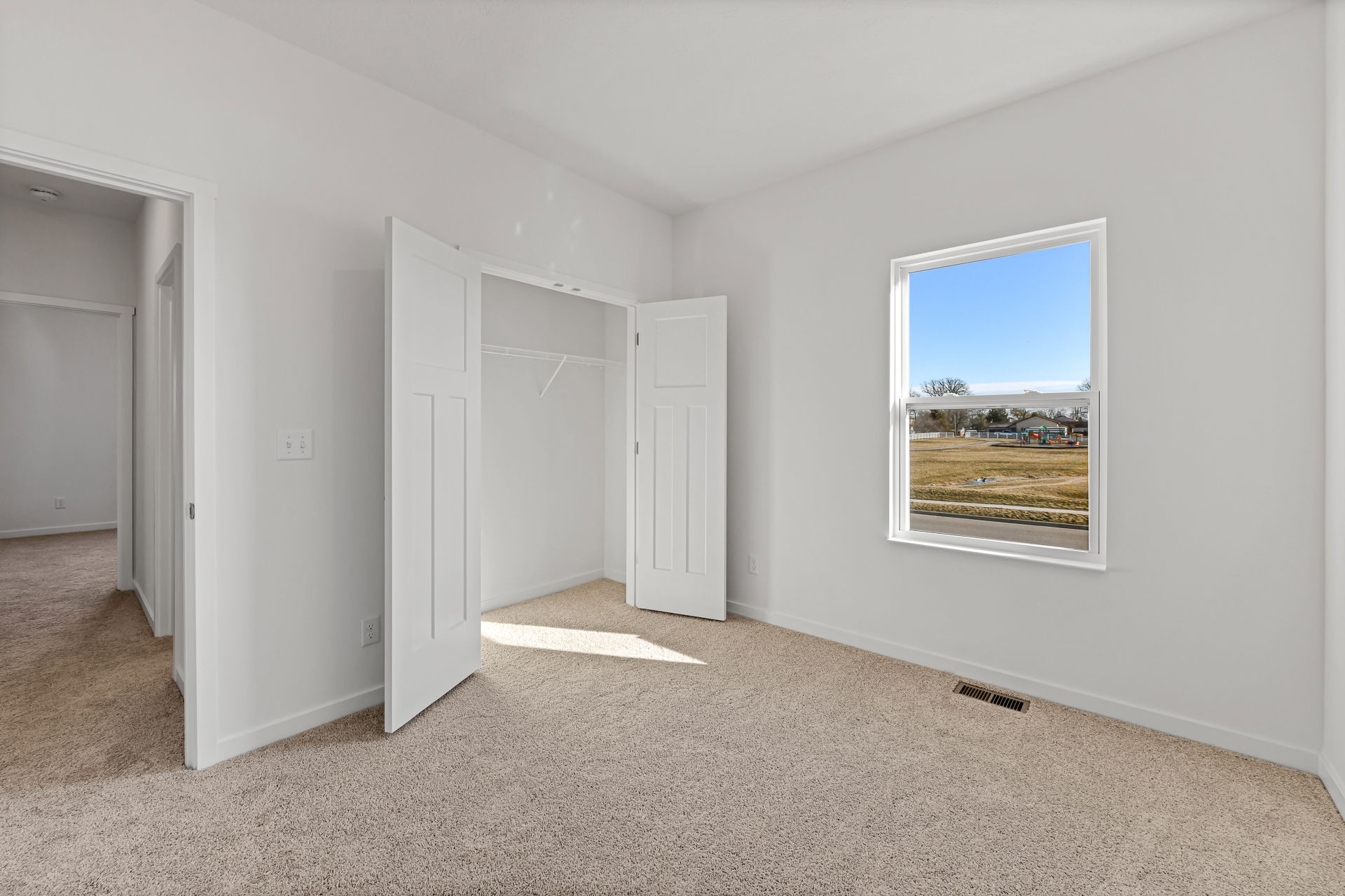 Empty, bright room with beige carpet, an open closet, and a window overlooking a grassy field.