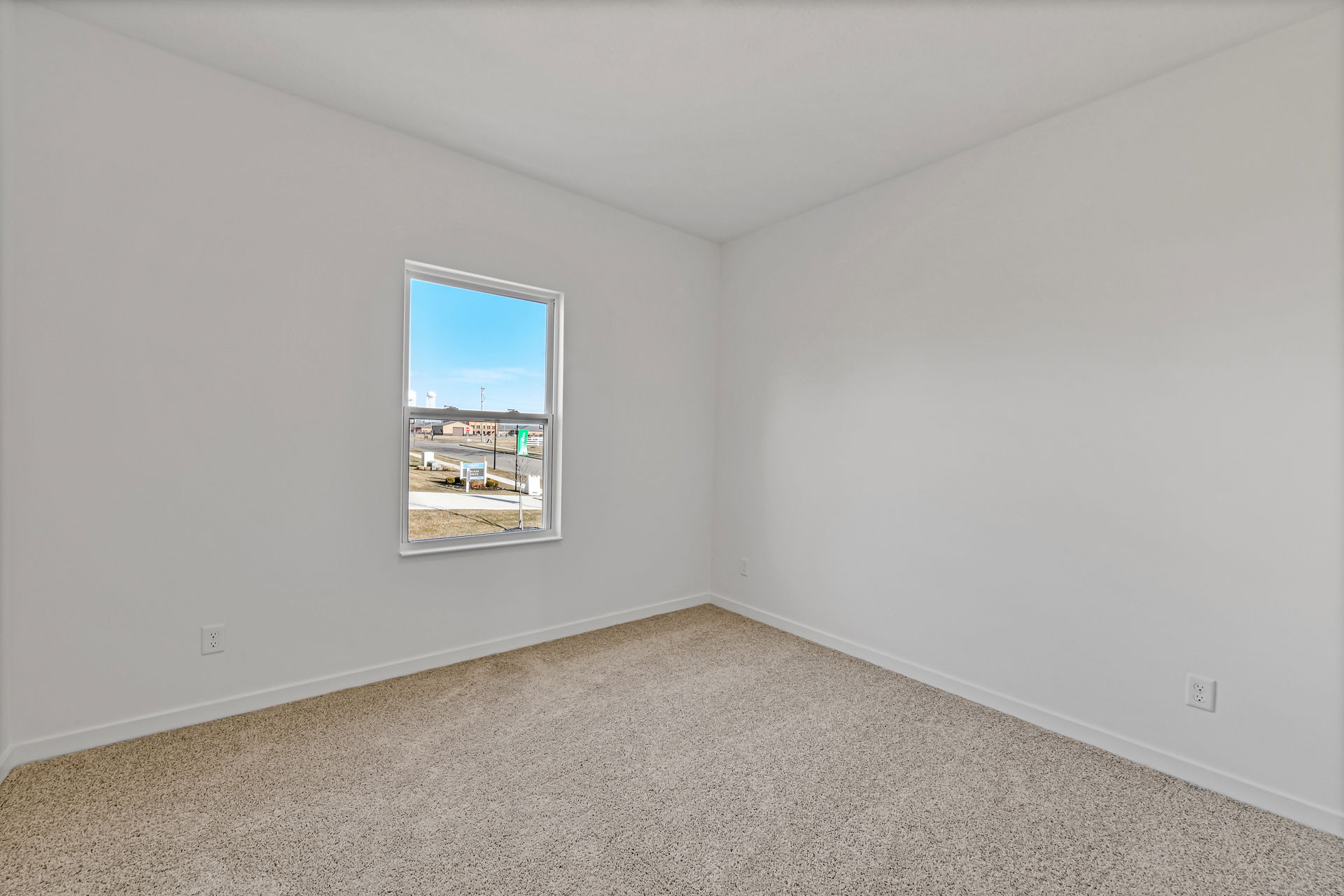 Empty room with beige carpet, white walls, and a window showcasing an exterior view.