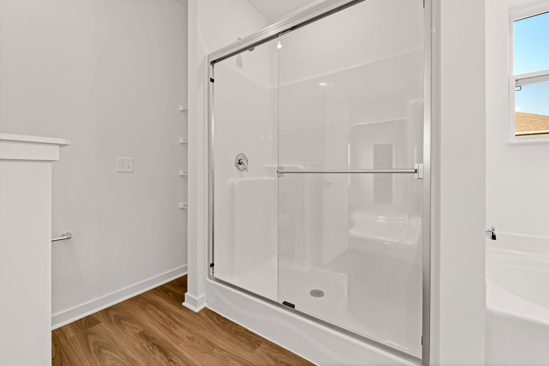 Modern bathroom with a sleek glass shower door, white walls, and wood-look flooring.