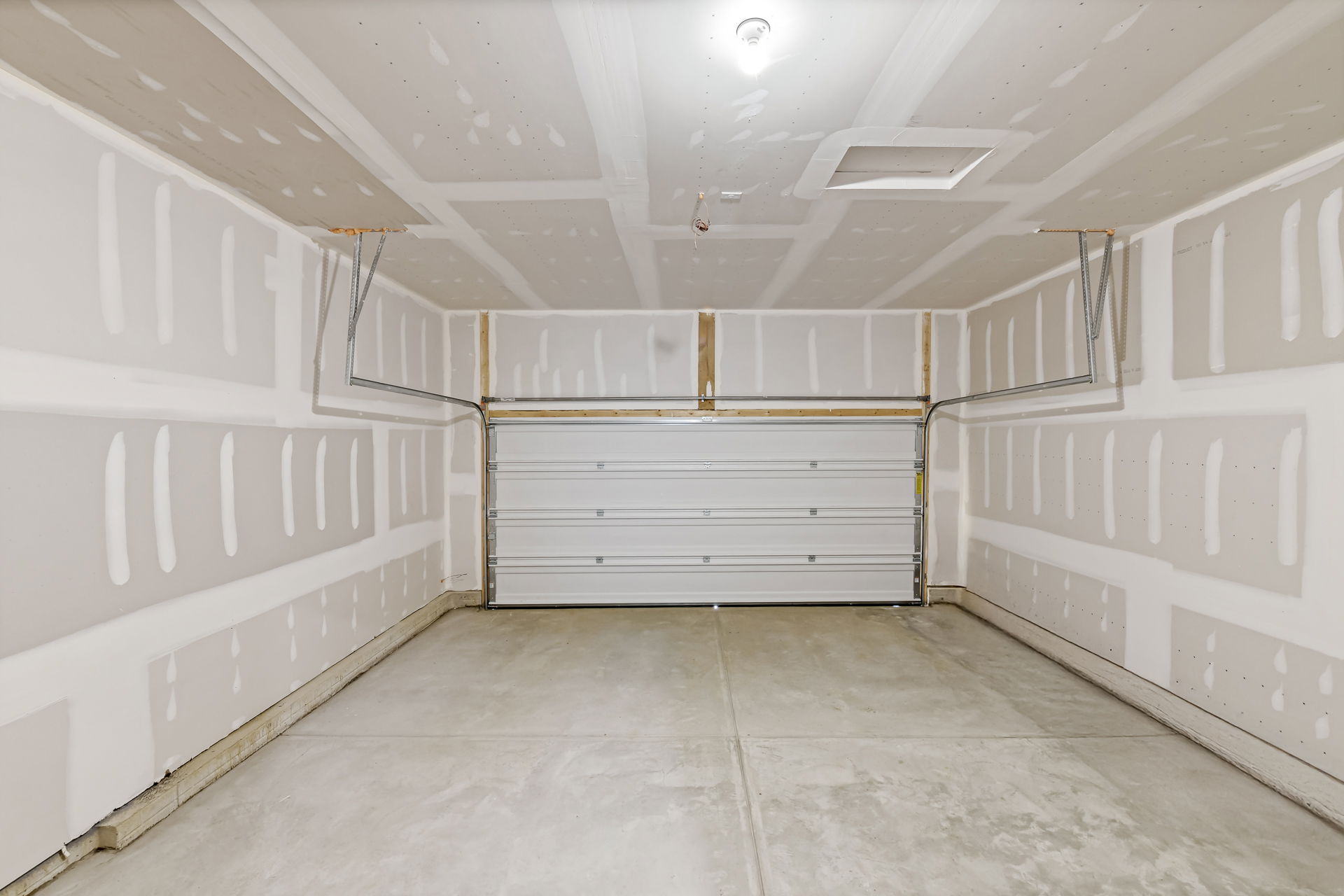 Empty unfinished garage interior with concrete floor and closed roll-up door.