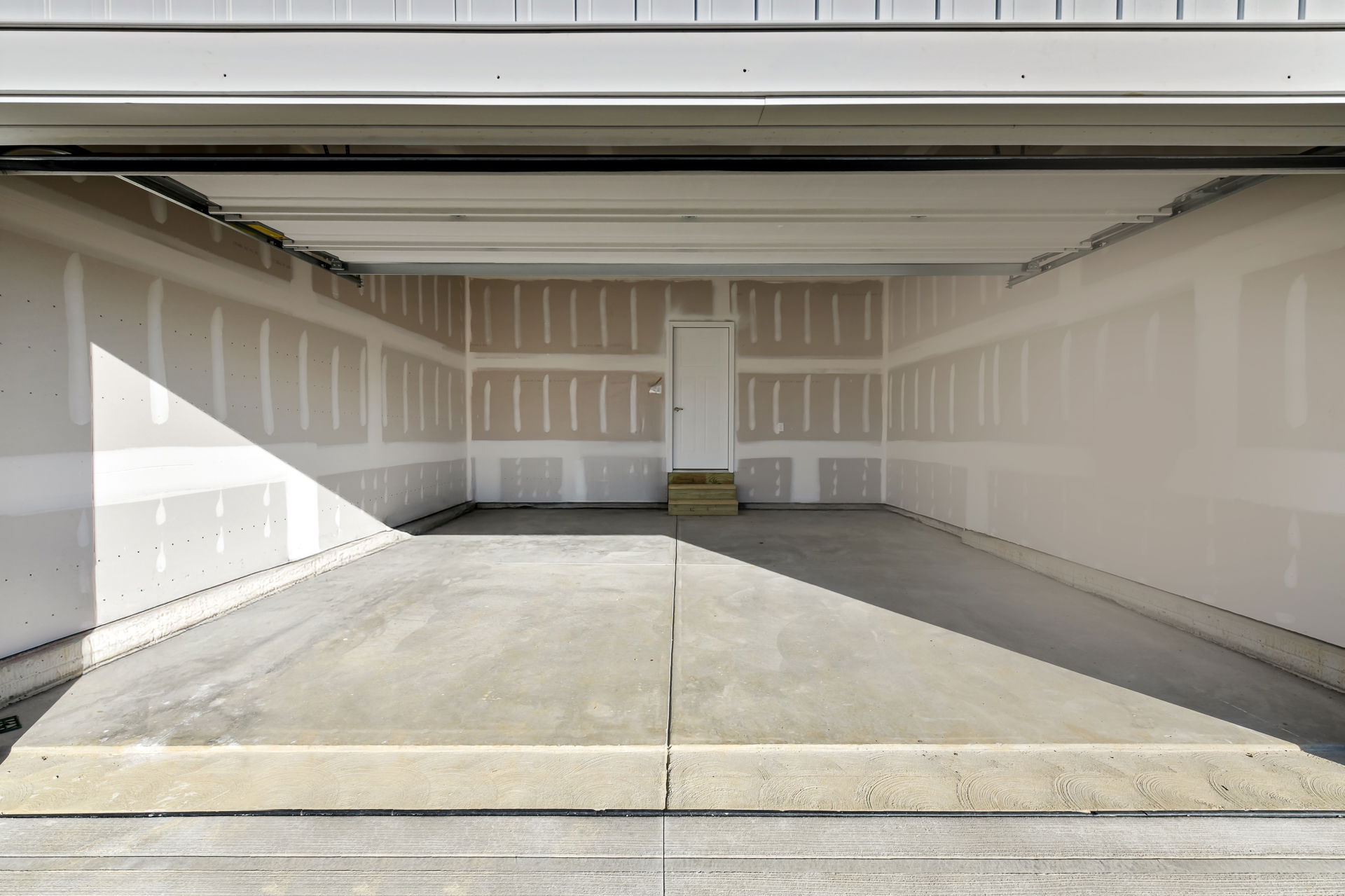 Empty two-car garage with open door, unfinished walls, and concrete flooring.