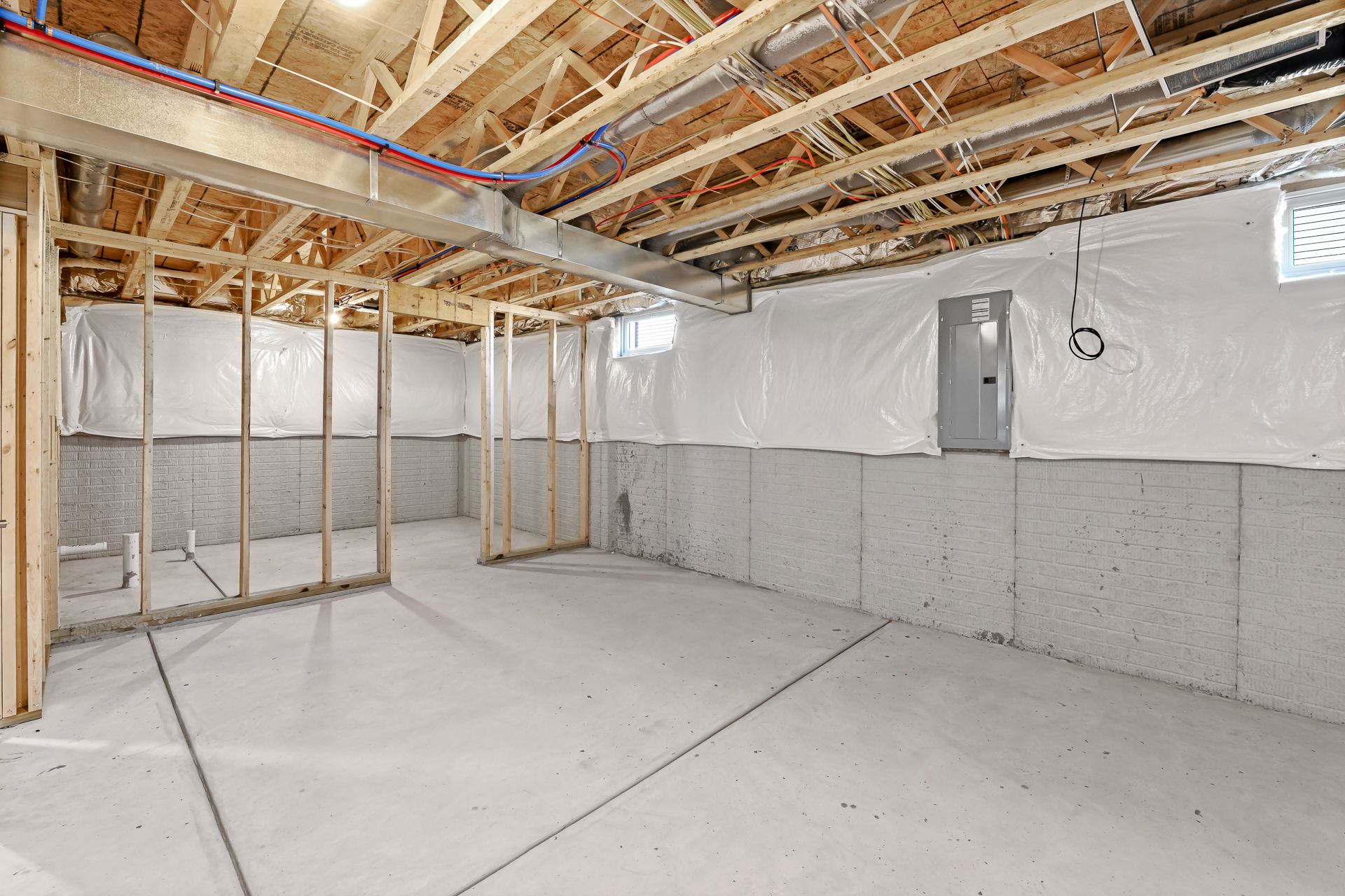 Unfinished basement area with exposed wooden beams, concrete walls, and partial framing, ready for renovation.