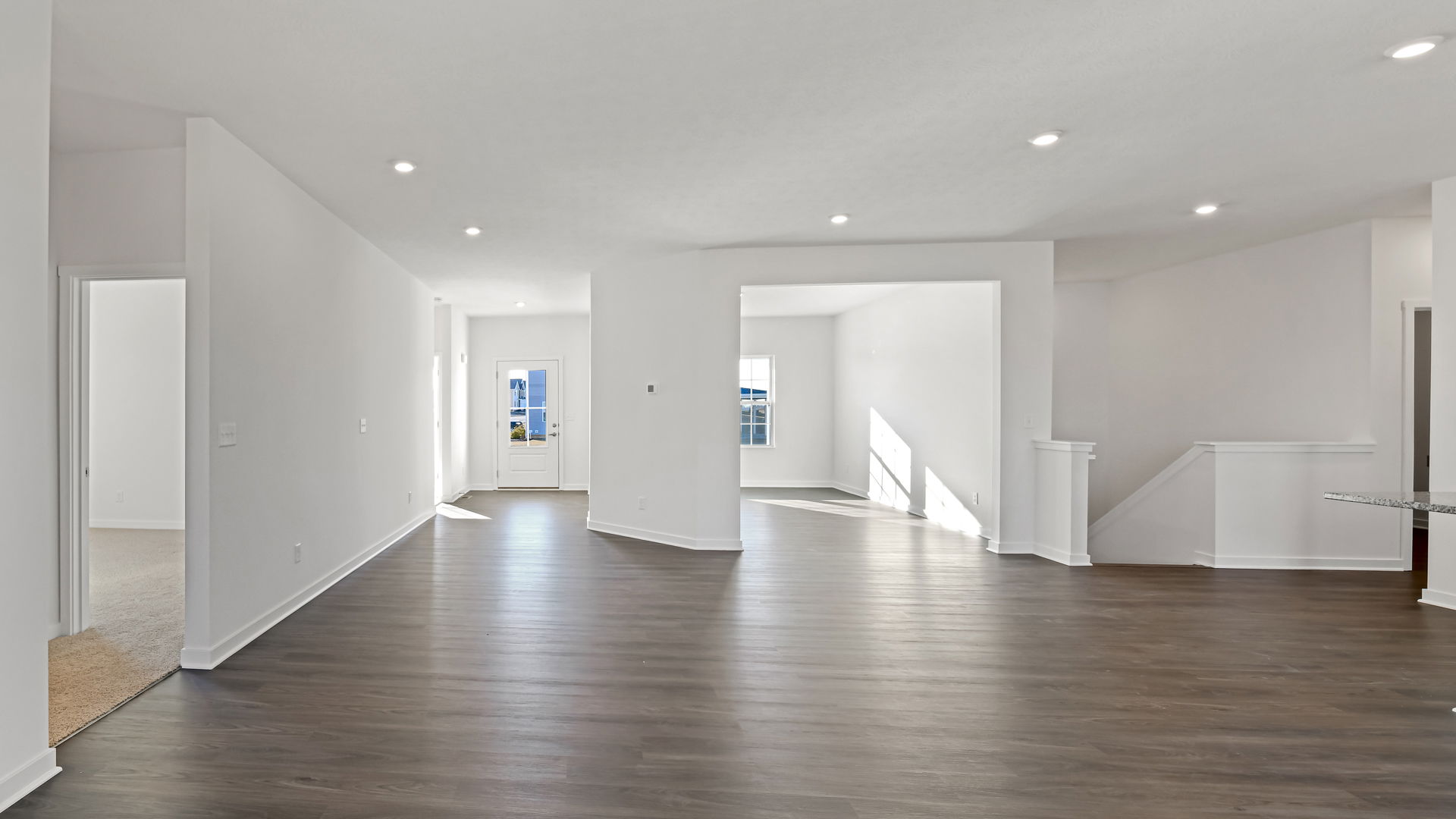 Spacious, modern open-layout home interior with hardwood flooring, bright natural lighting, and neutral-colored walls.