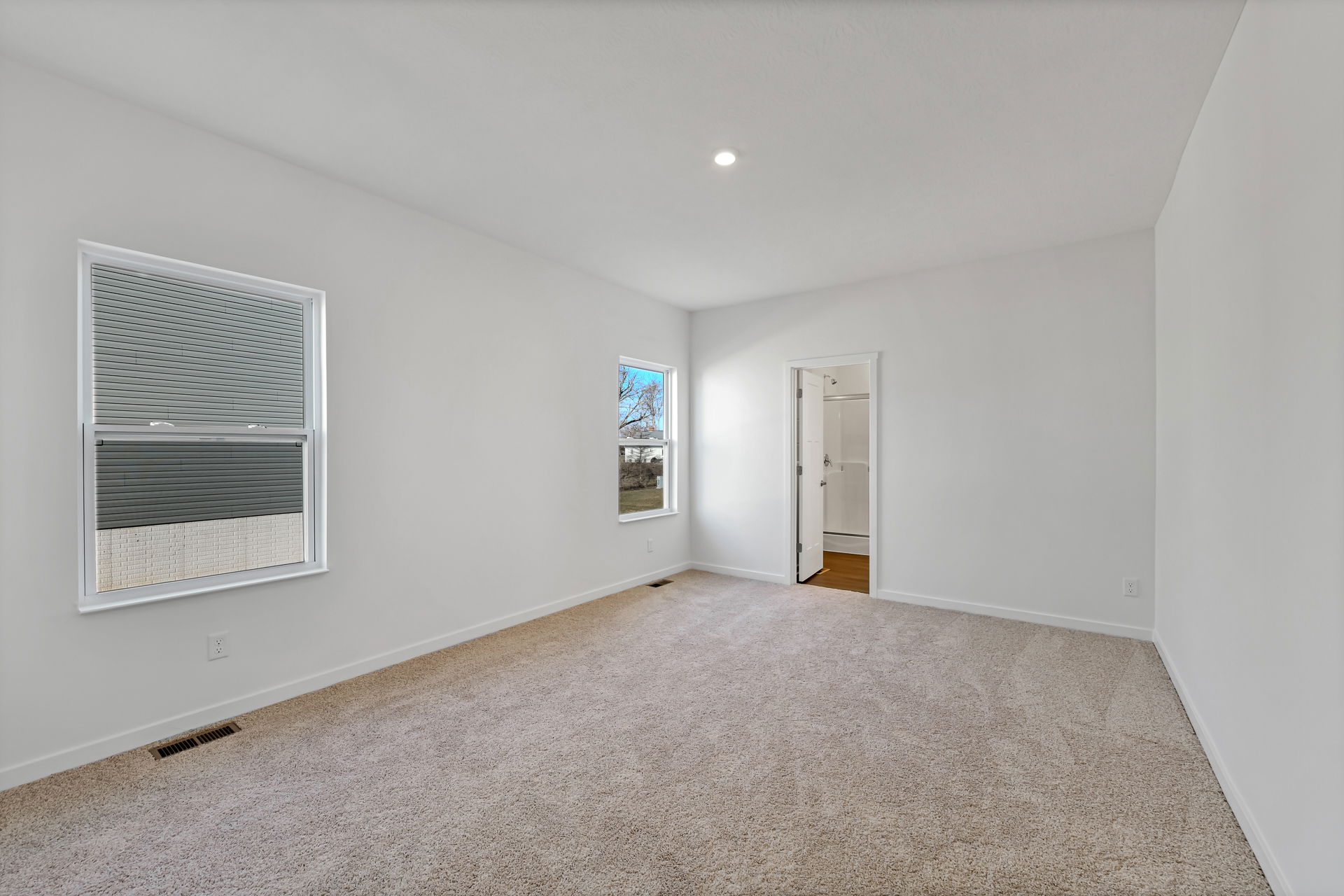 Spacious bedroom with carpet flooring, two windows, and an attached bathroom in a modern house.
