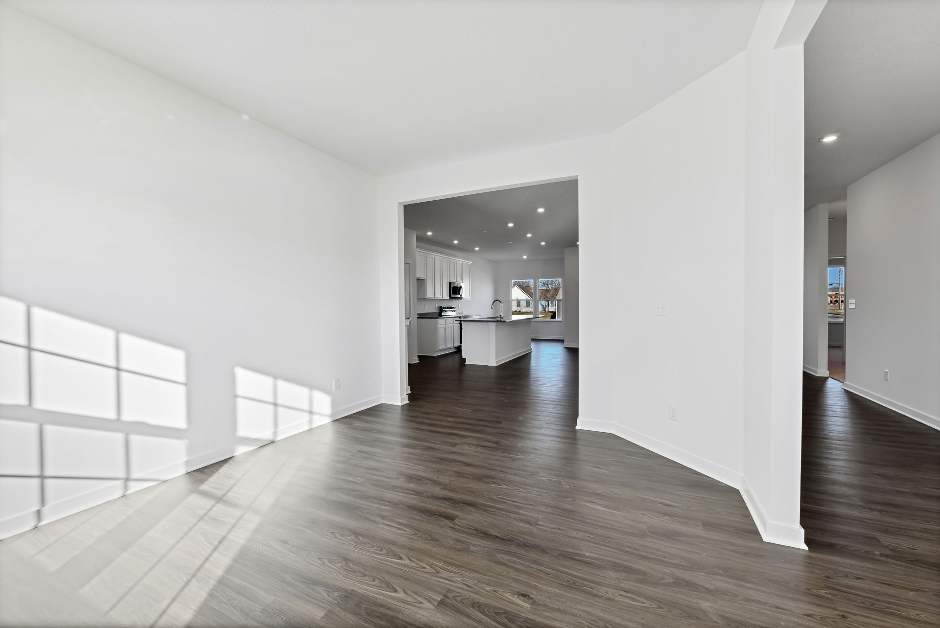 Bright, modern open-concept living space with hardwood floors leading to a kitchen area with white cabinetry.