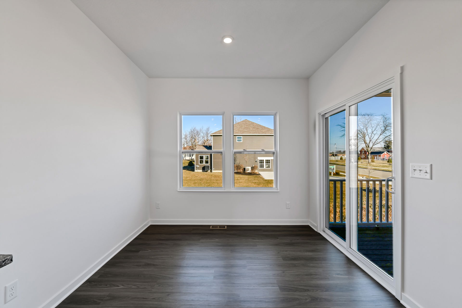 Empty room with large windows and sliding glass door showcasing a clear view of a suburban backyard and neighboring house.