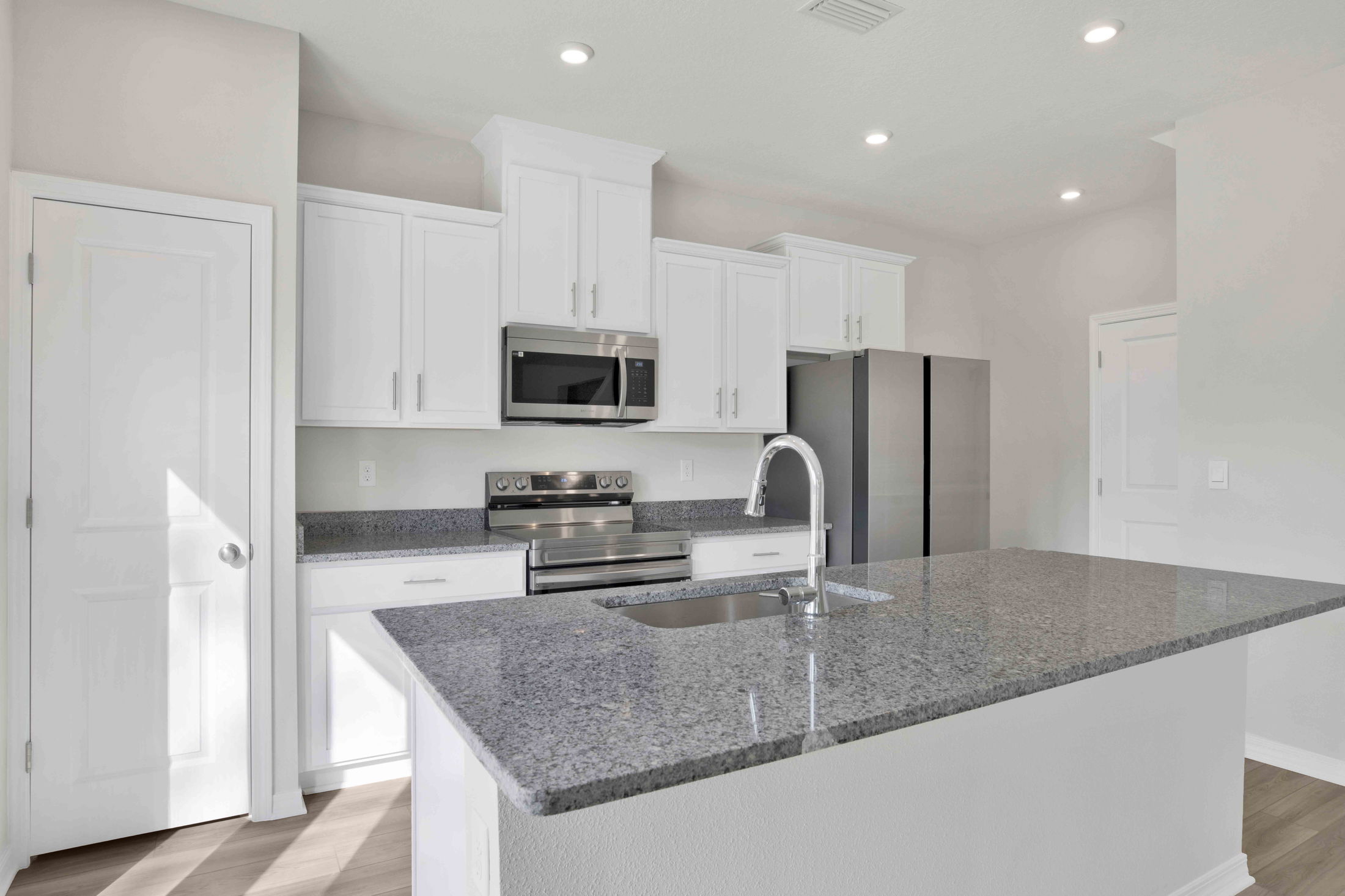 Modern kitchen with white cabinetry, stainless steel appliances, and granite countertops.