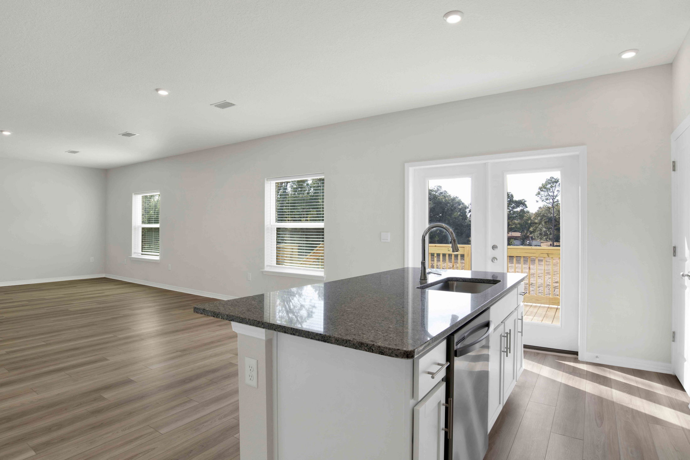 Modern open-plan kitchen and living area with granite countertops, hardwood floors, and large windows overlooking a deck.