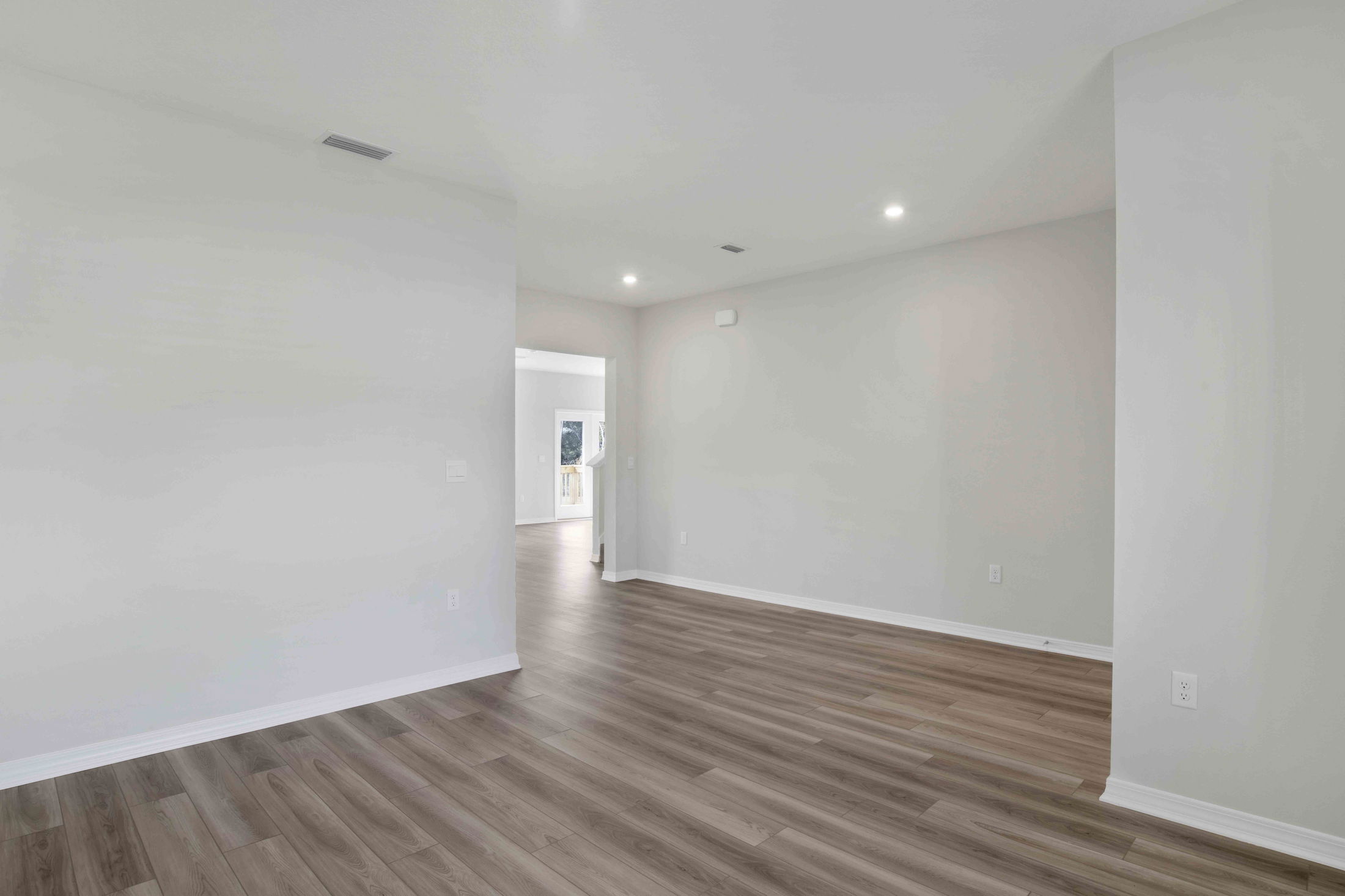 Empty modern room with light hardwood floors, neutral walls, and recessed lighting leading to an open doorway.
