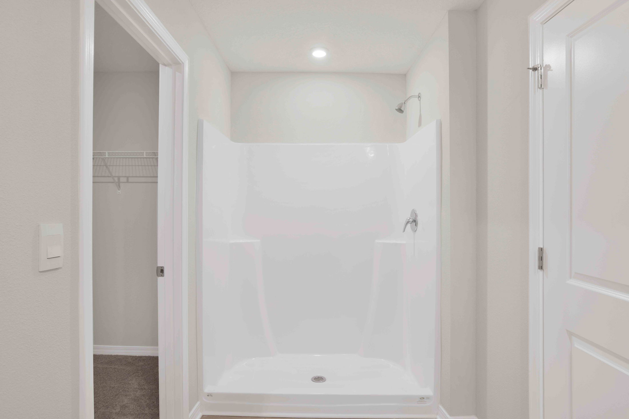 Minimalist white alcove shower with high-gloss acrylic walls and chrome fixtures in a modern bathroom setting.