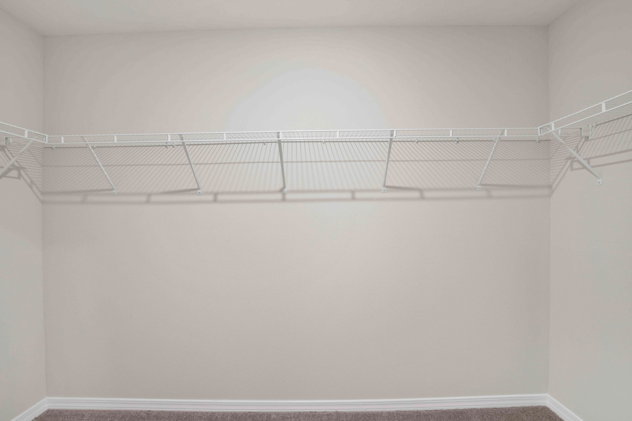 Empty walk-in closet with light gray walls and a white wire shelf.