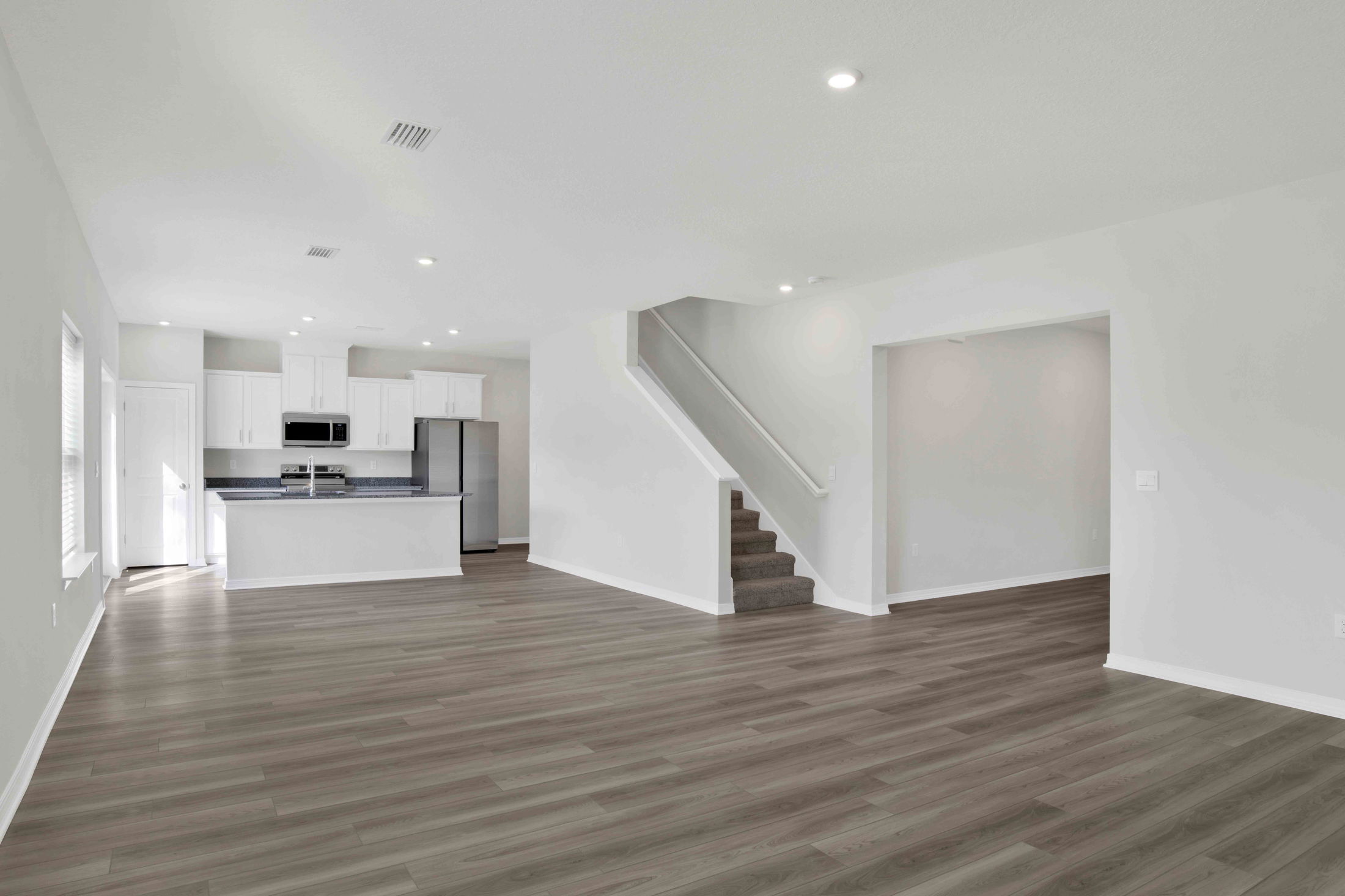 Spacious modern living room with hardwood floors, open kitchen, and staircase leading to upper level.