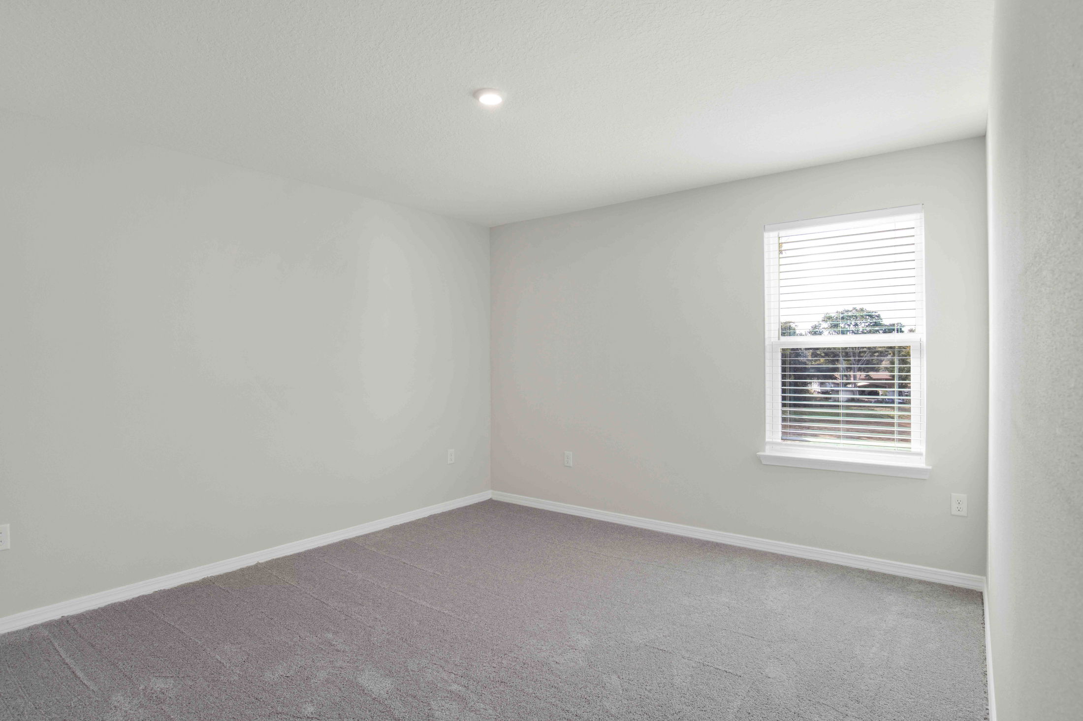 Empty room with gray carpet and a window with blinds allowing natural light.