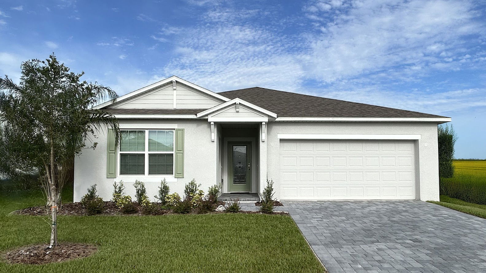 Modern single-story white house with a two-car garage and landscaped front yard against a blue sky backdrop.