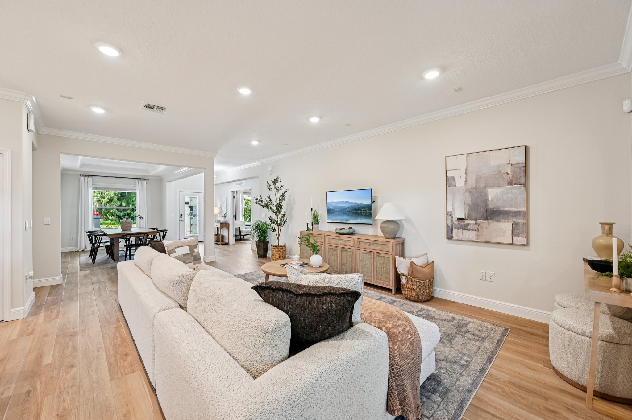 Modern open-concept living room with beige sofa, wall-mounted TV, wood flooring, and adjoining dining area.