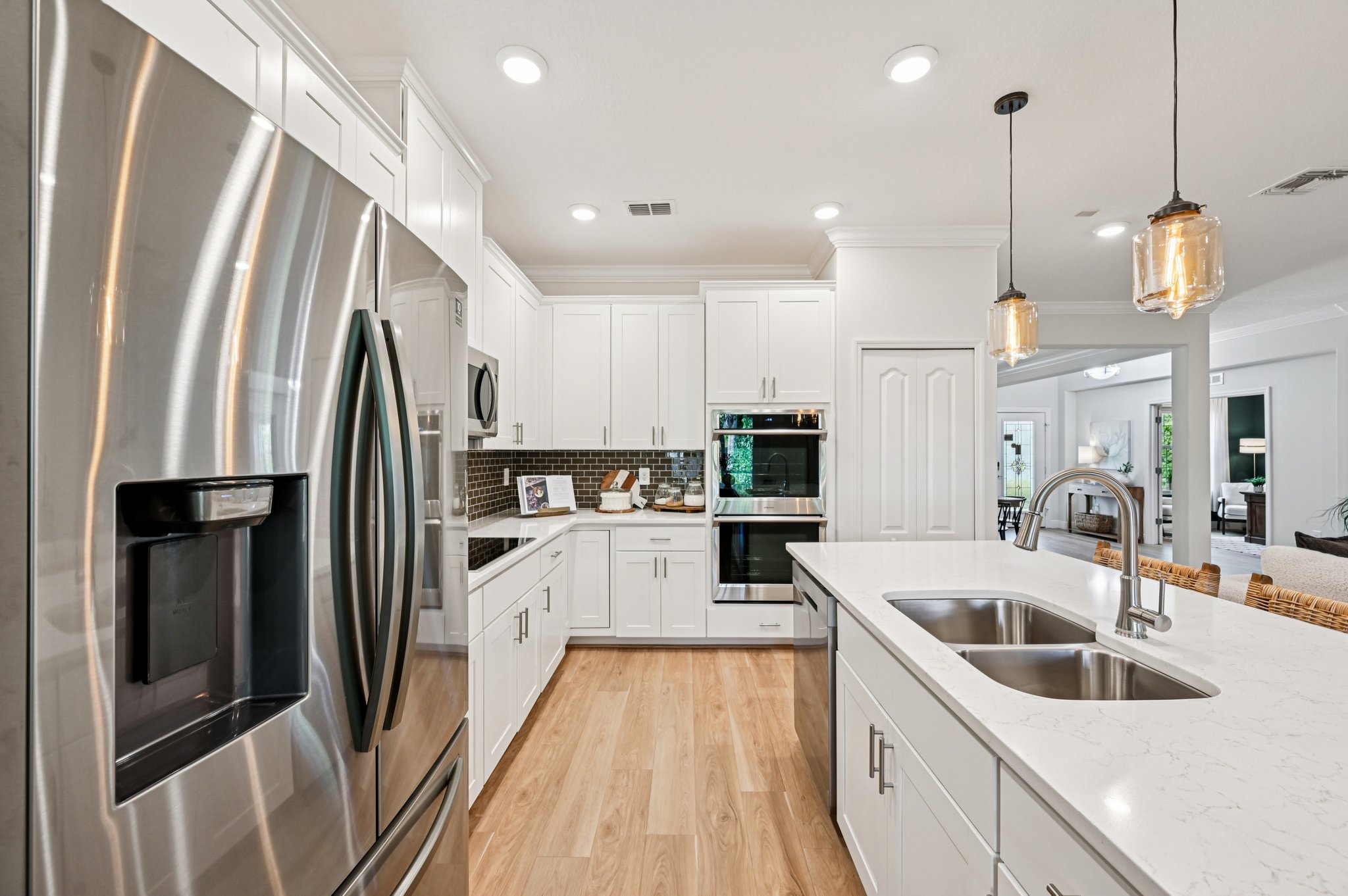 Modern kitchen with stainless steel appliances, white cabinets, and a central island with a double sink under pendant lighting.