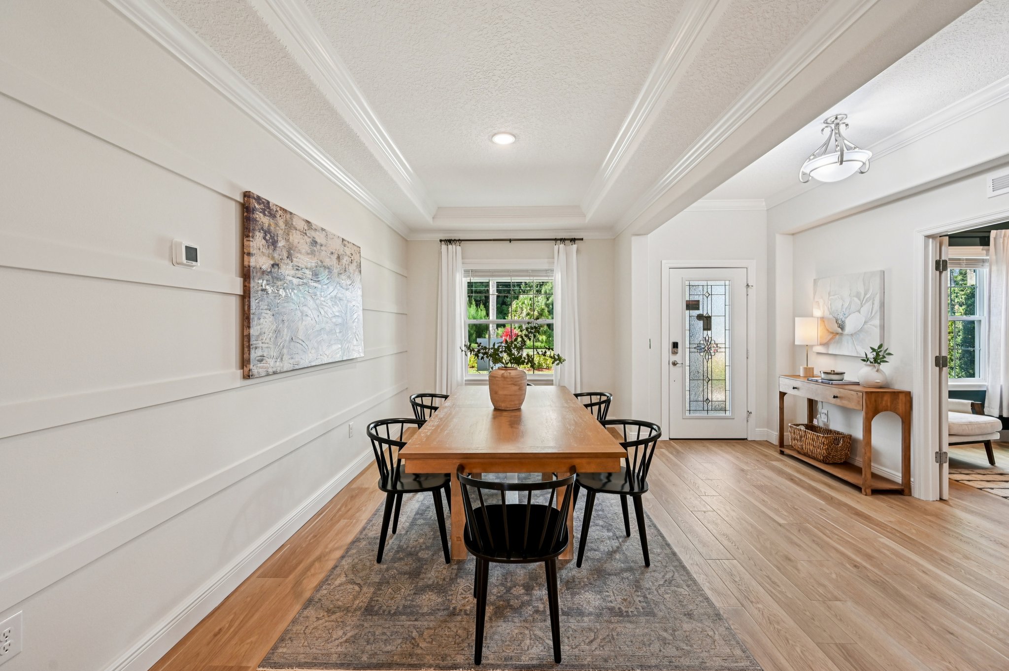 Modern dining room with a wooden table, black chairs, and elegant decor including wall art and plants.