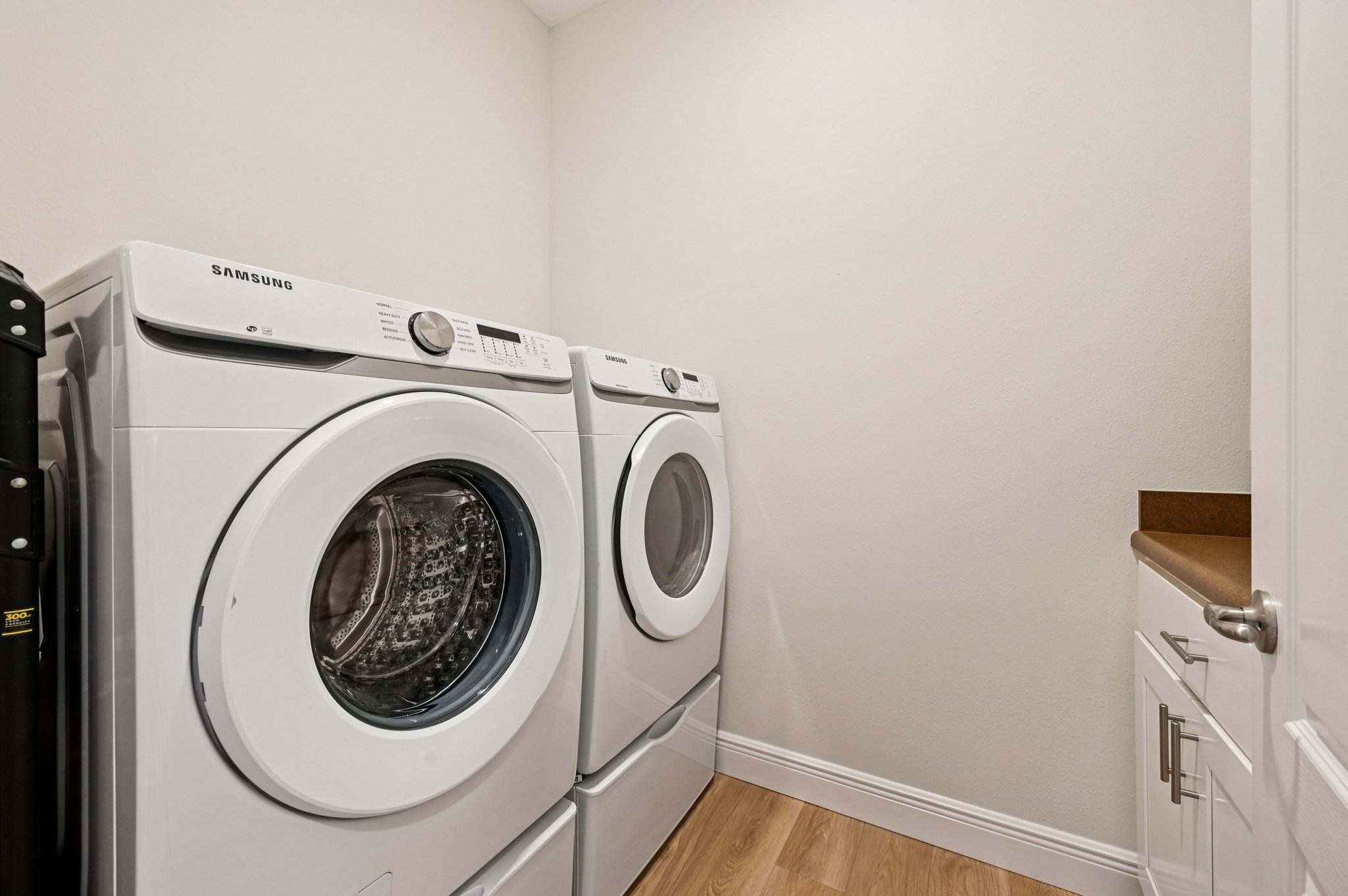 Front-loading Samsung washer and dryer set in a modern laundry room with wooden flooring.