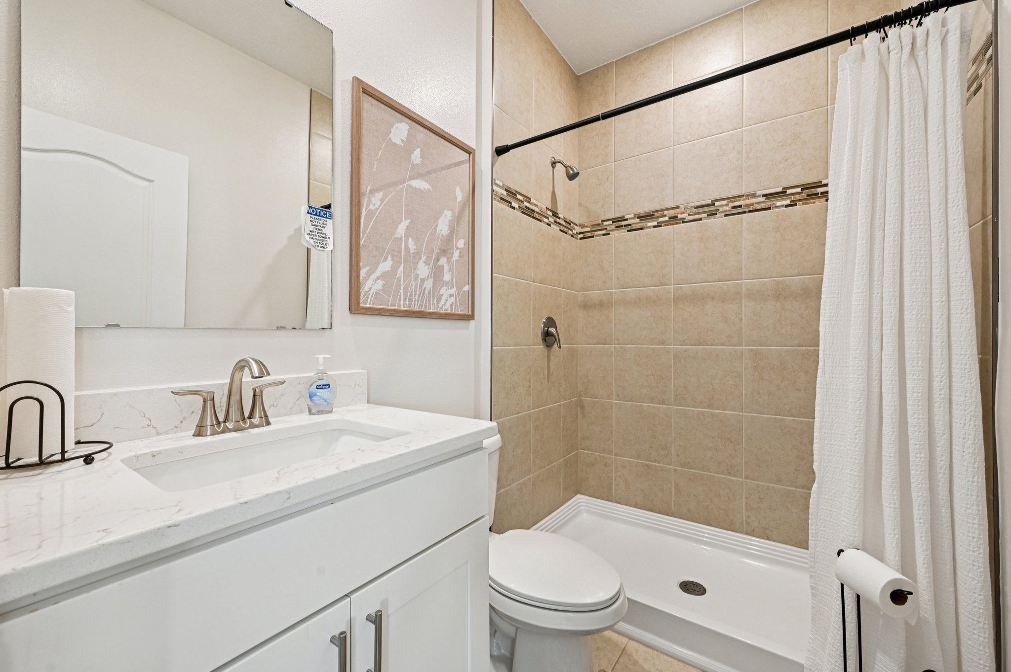 Contemporary bathroom featuring a white vanity with marble countertop, beige tiled shower with decorative border, and modern fixtures.