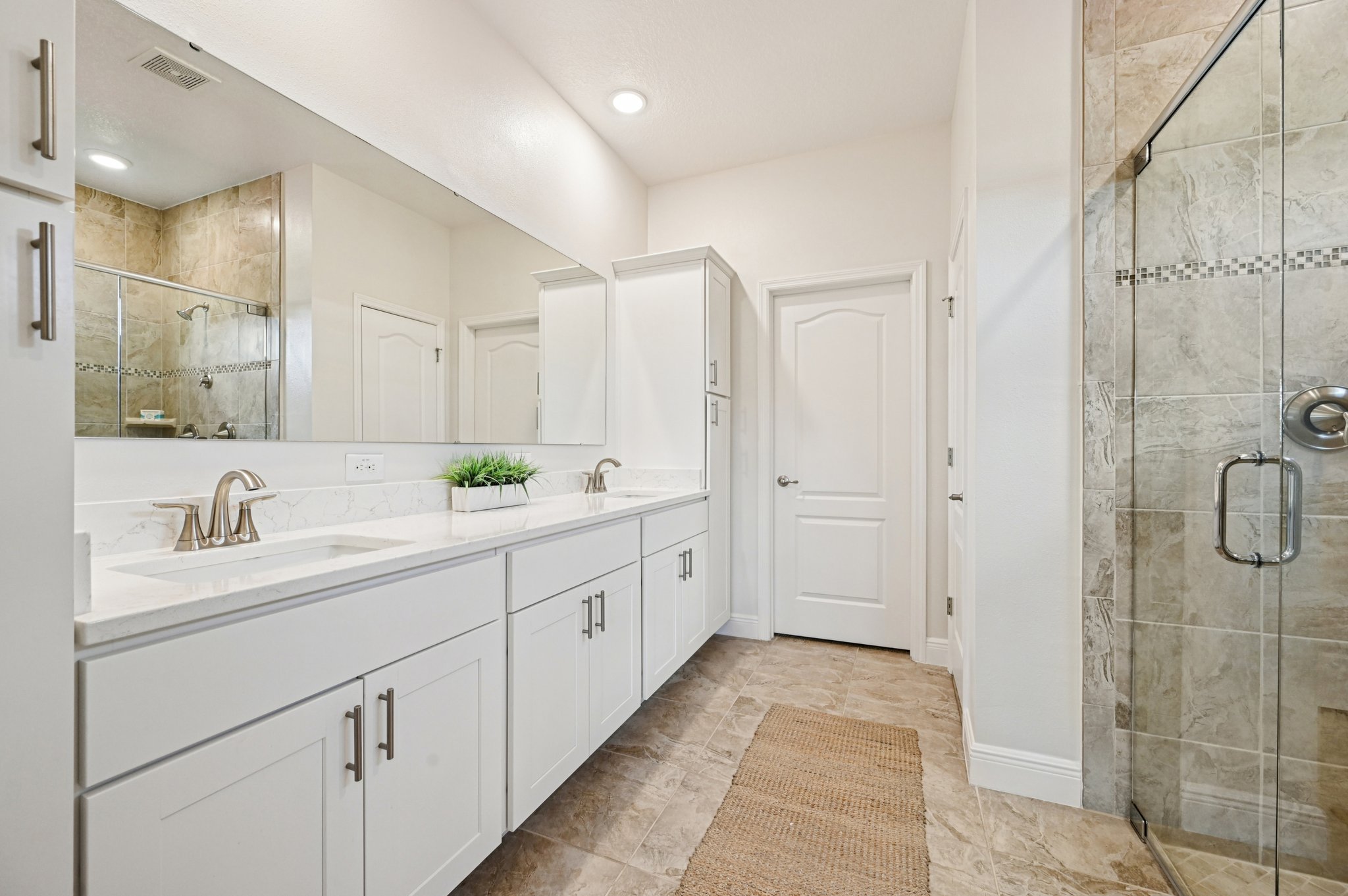 Modern bathroom with double sink vanity, large mirror, and glass-enclosed shower.
