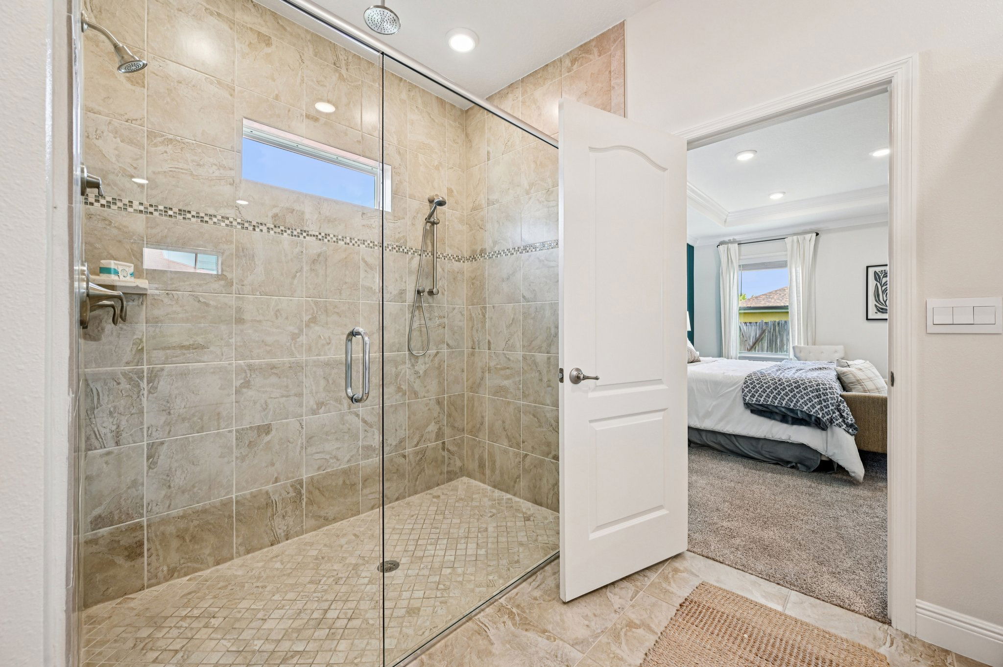 Elegant bathroom with a large glass-enclosed walk-in shower and stone tile design, opening into a modern, cozy bedroom.