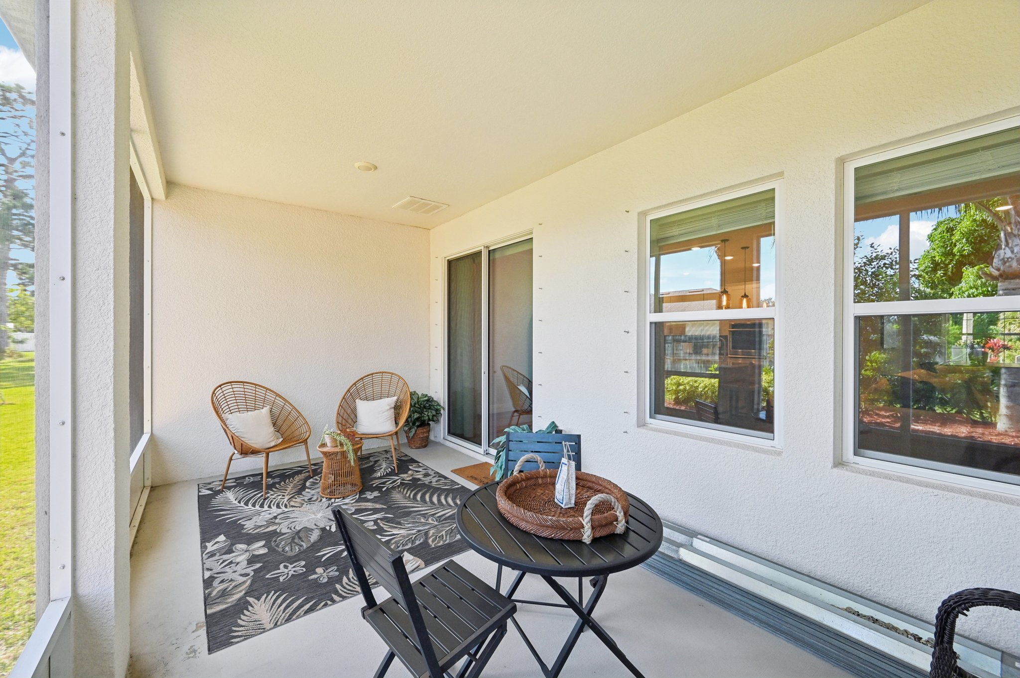 Stylish and cozy screened-in porch with wicker chairs, a small black table, and a decorative rug, perfect for outdoor relaxation.