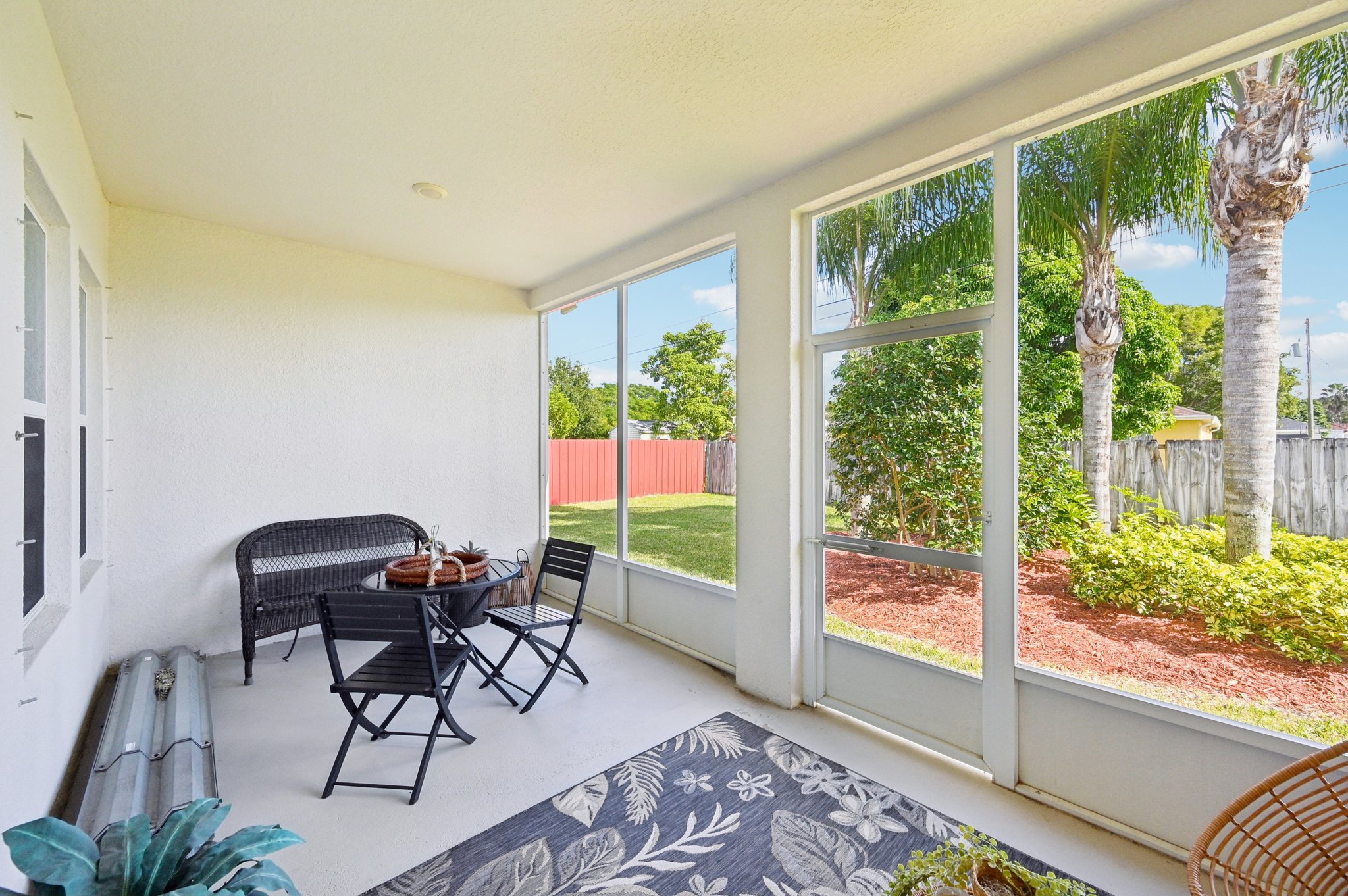 Sunlit screened porch with black patio furniture and a view of a lush, landscaped backyard.