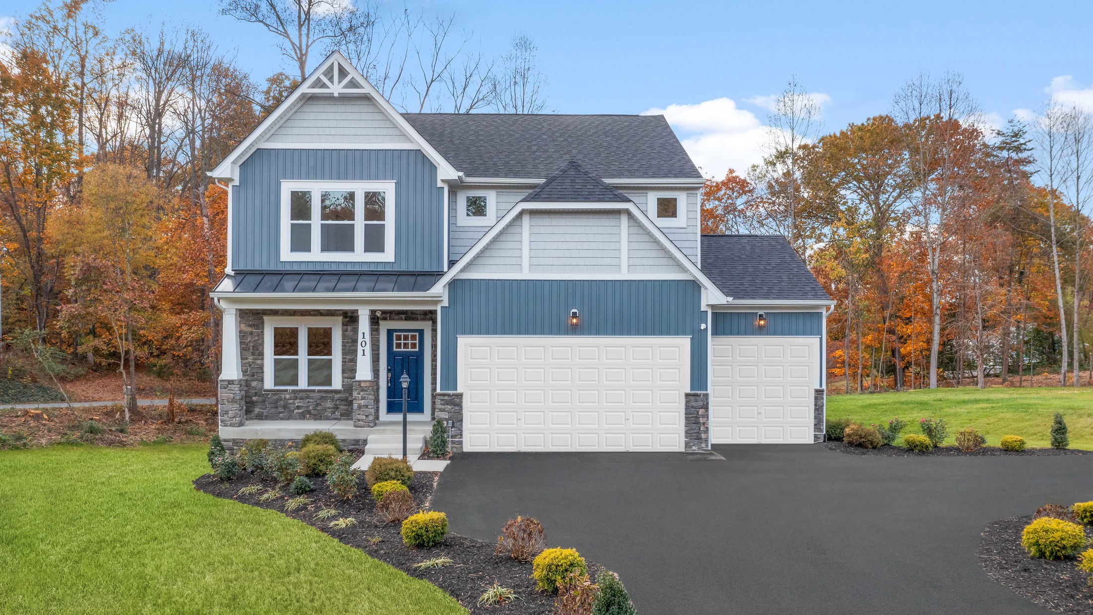 Modern two-story blue house with a double garage, surrounded by autumn trees and landscaped yard.