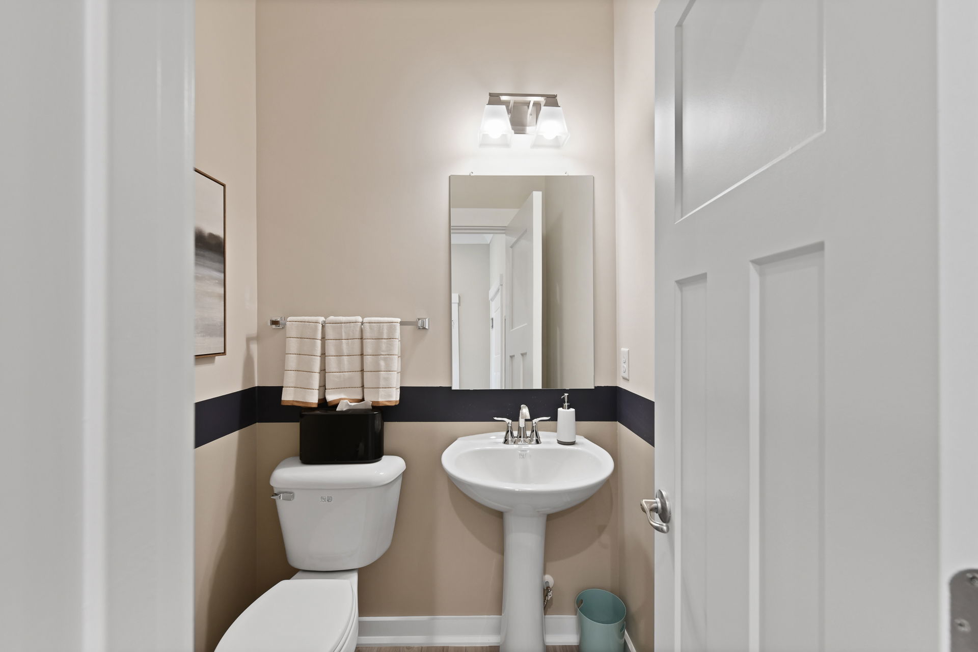 A small, modern bathroom with a pedestal sink, wall-mounted mirror, and neutral decor.