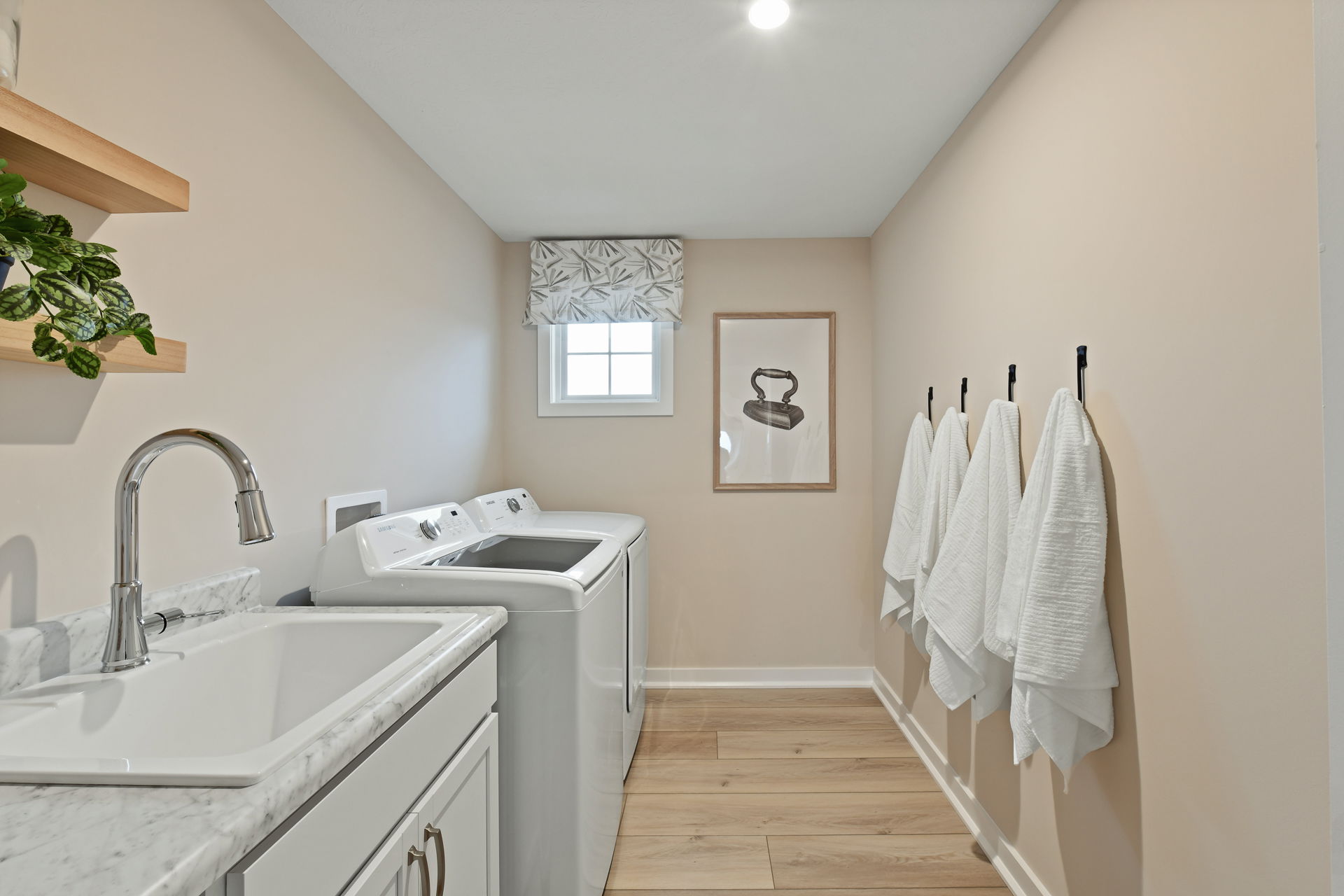 Modern laundry room with a marble countertop, sink, washer and dryer, and neatly hung white towels.