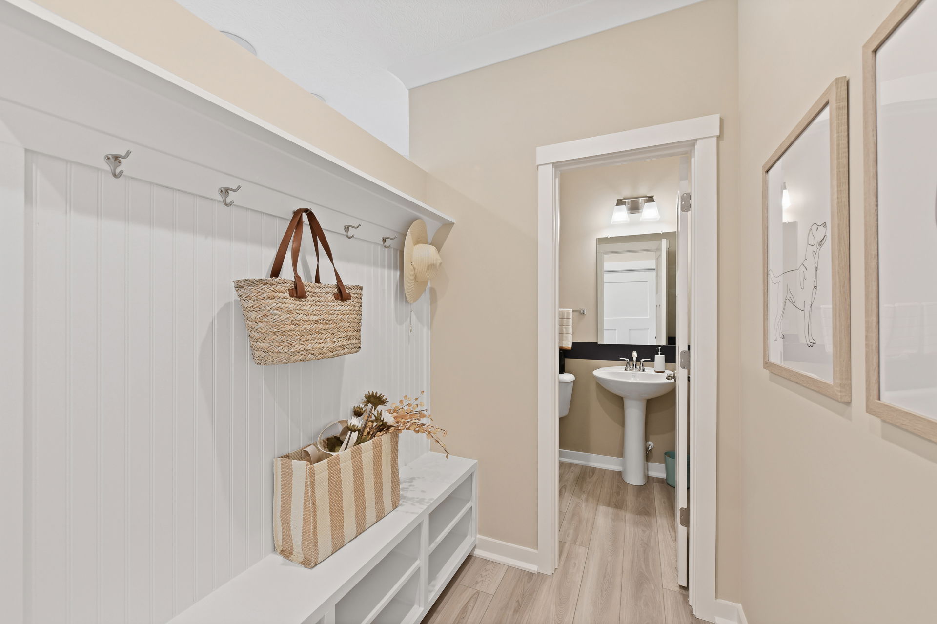 Bright mudroom entryway with wall hooks, storage benches, and a view into a modern bathroom with a pedestal sink.