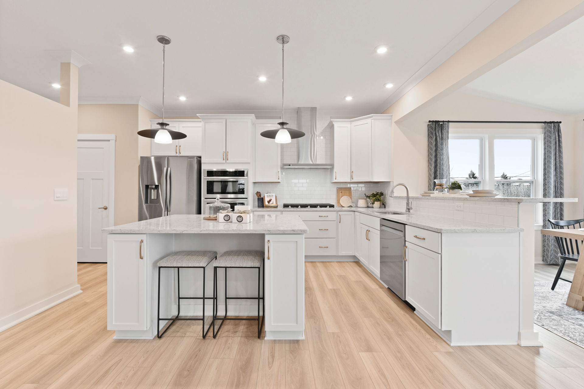 Modern kitchen with white cabinetry, marble countertops, stainless steel appliances, and pendant lighting over a central island.