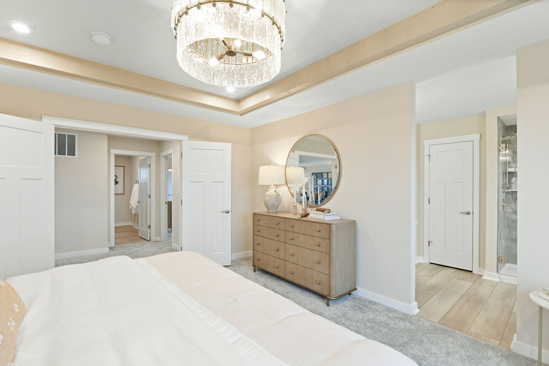 Luxurious bedroom with elegant chandelier, wooden dresser, and modern decor.