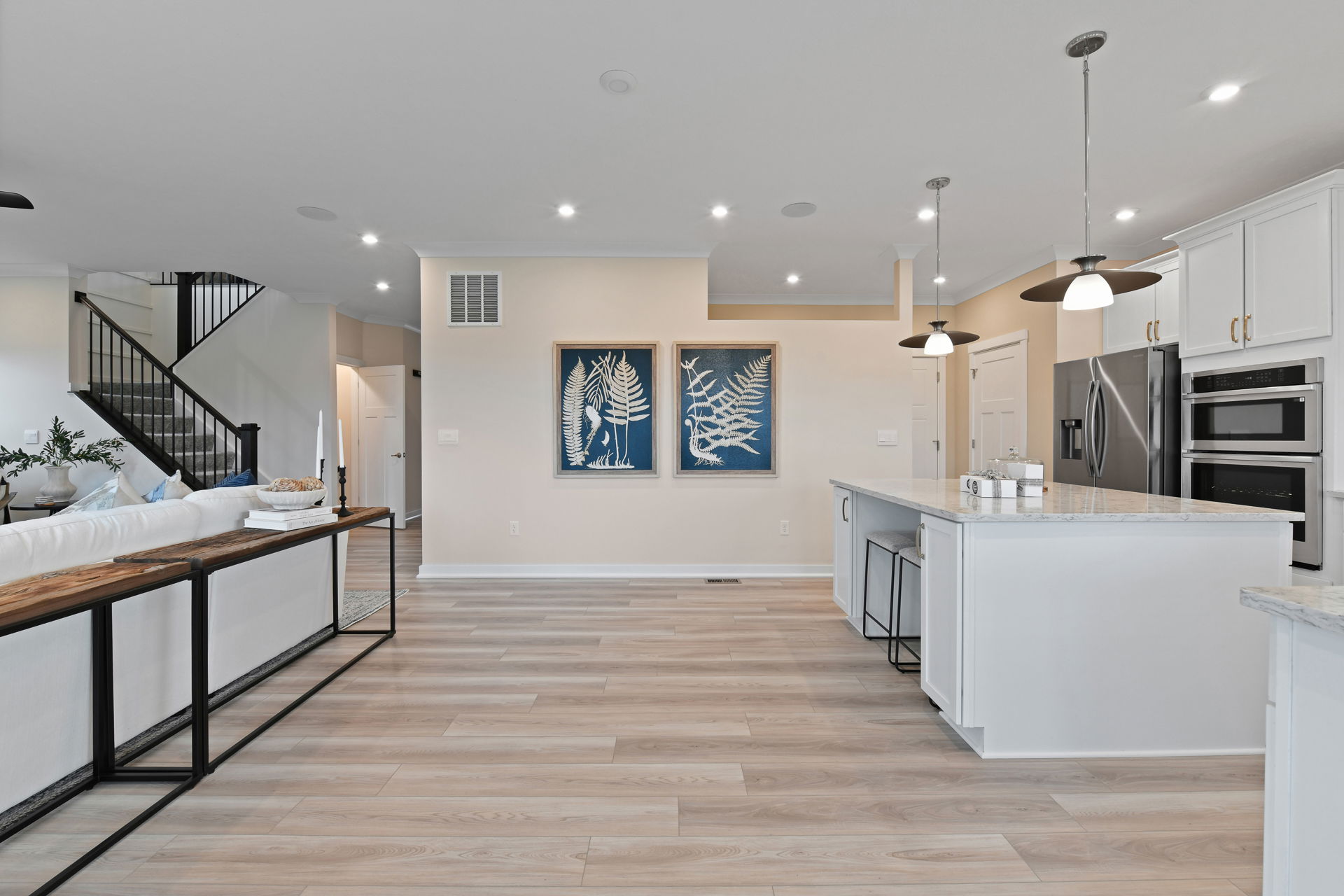 Modern open-concept kitchen with a large island, white cabinets, stainless steel appliances, and decorative fern artwork on the wall.