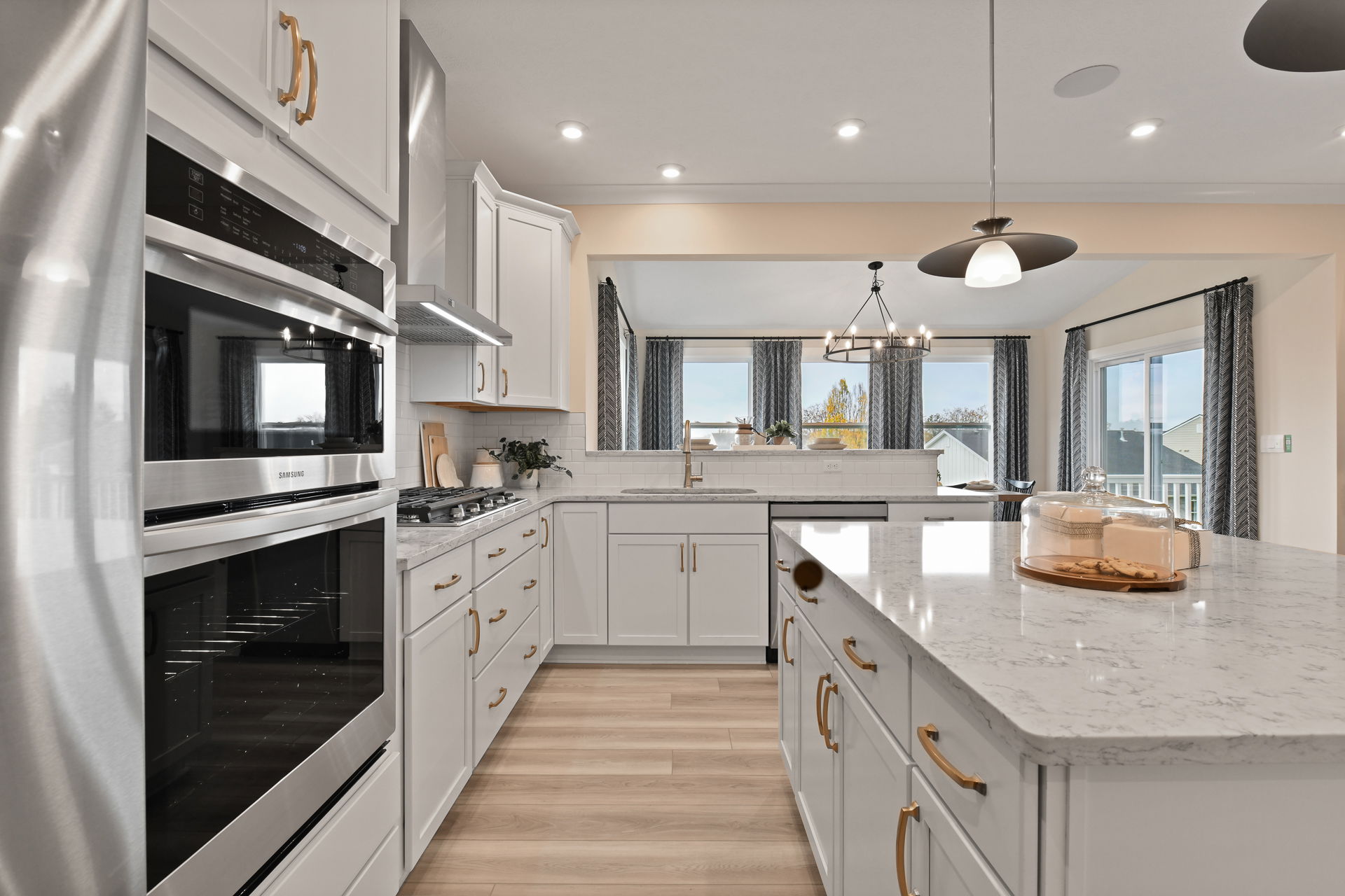 Modern kitchen interior with white cabinets, marble countertops, stainless steel appliances, and a central island under stylish lighting.