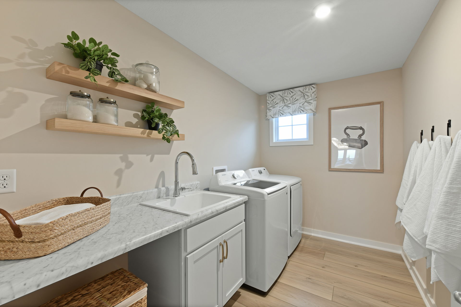 Modern laundry room with white washer and dryer, marble countertop with sink, decorative shelving, and wooden flooring.