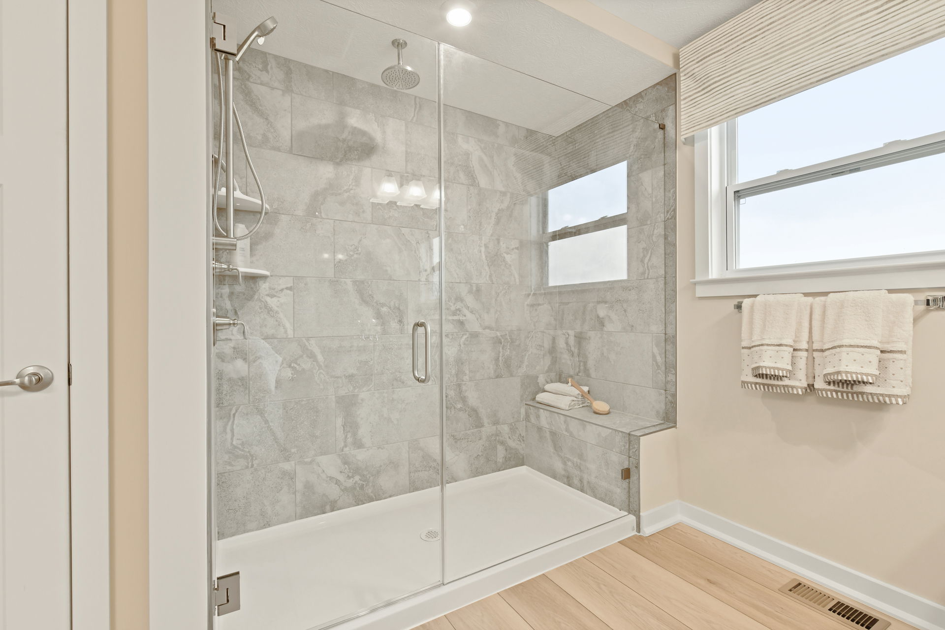 Modern bathroom with a sleek glass-enclosed shower featuring gray marble tiles and adjacent towel rack.