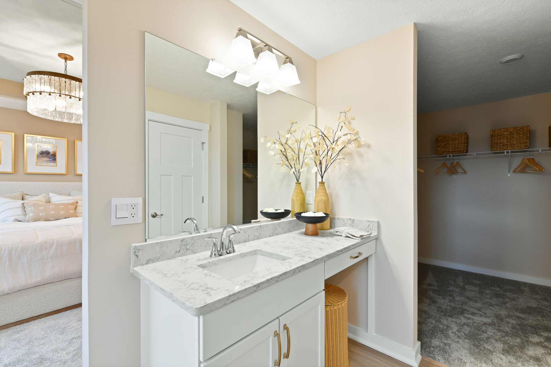 Elegant bathroom vanity featuring marble countertop, decorative vases with white flowers, and adjacent walk-in closet with wicker baskets and hangers.