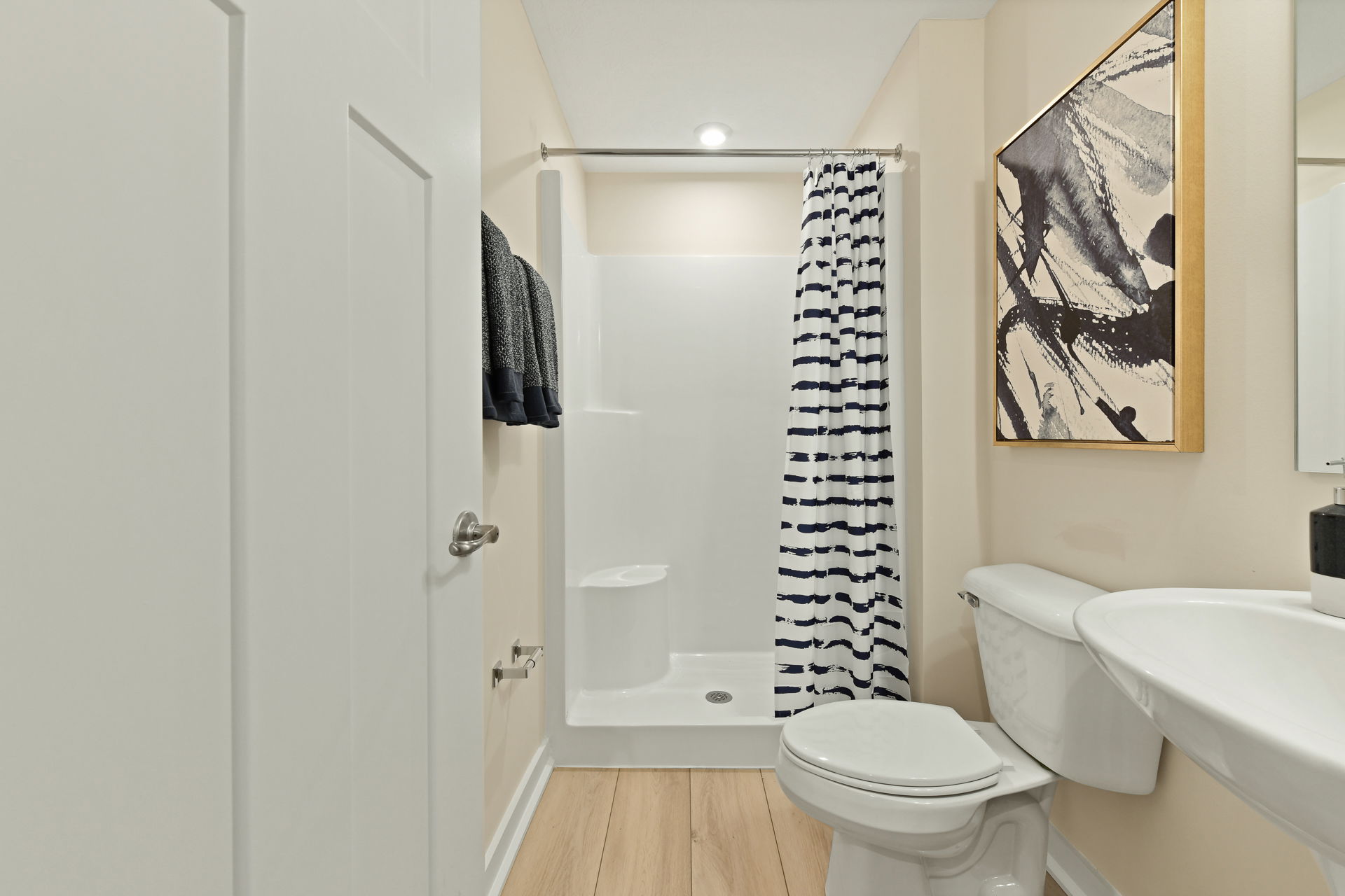 Modern bathroom with white walls, a striped shower curtain, and contemporary artwork.