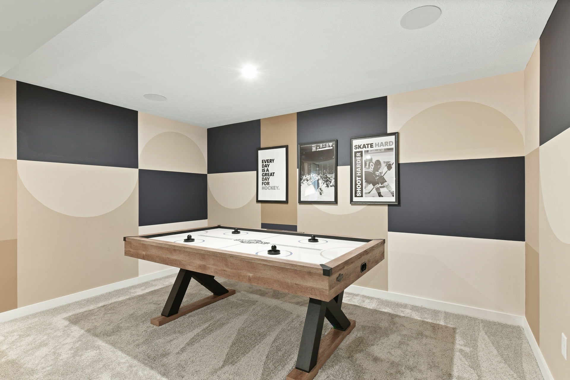 Modern basement game room featuring an air hockey table, geometric wall design, and hockey-themed decor.
