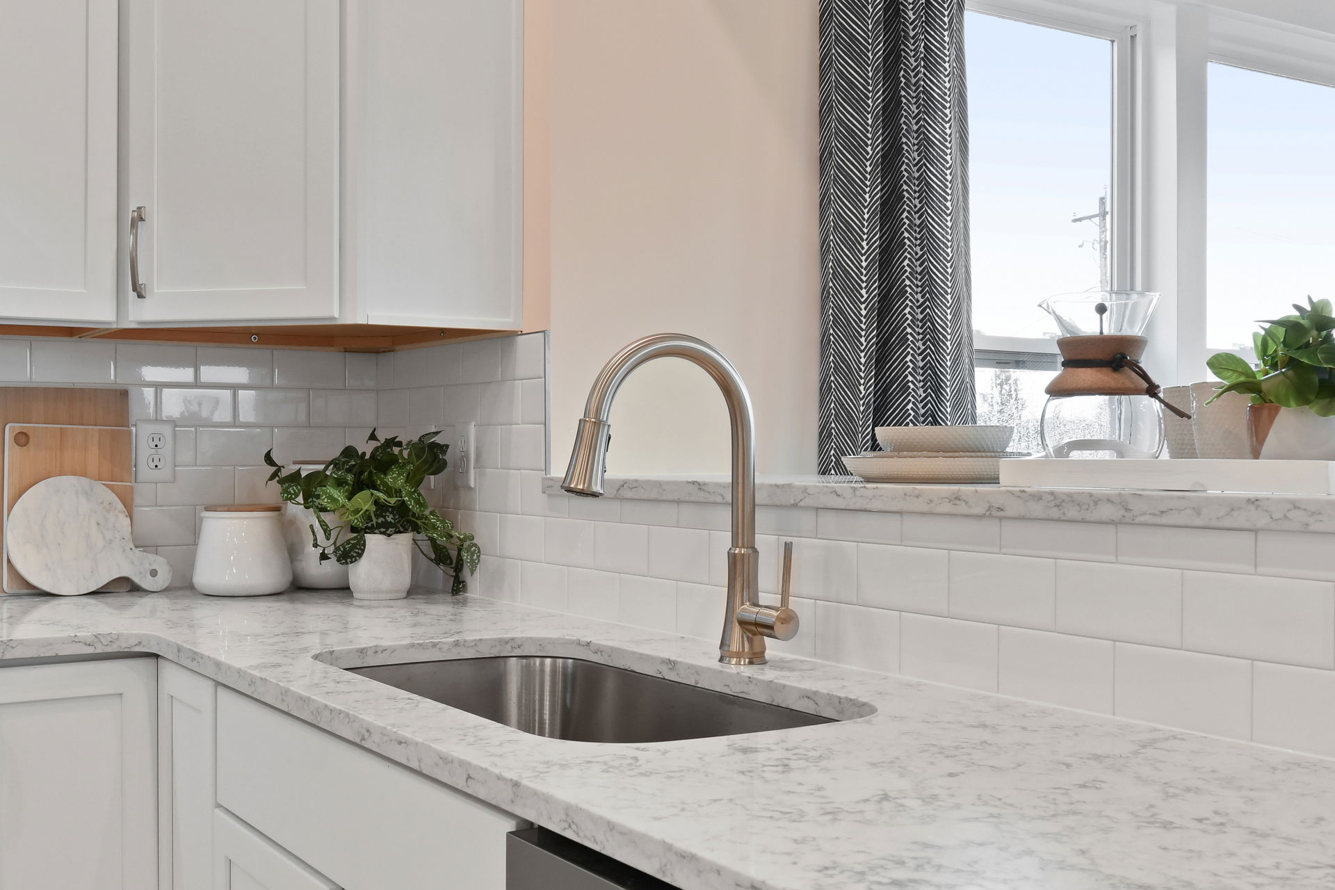 Modern kitchen with white cabinets, marble countertops, and a stainless steel sink with a sleek faucet.