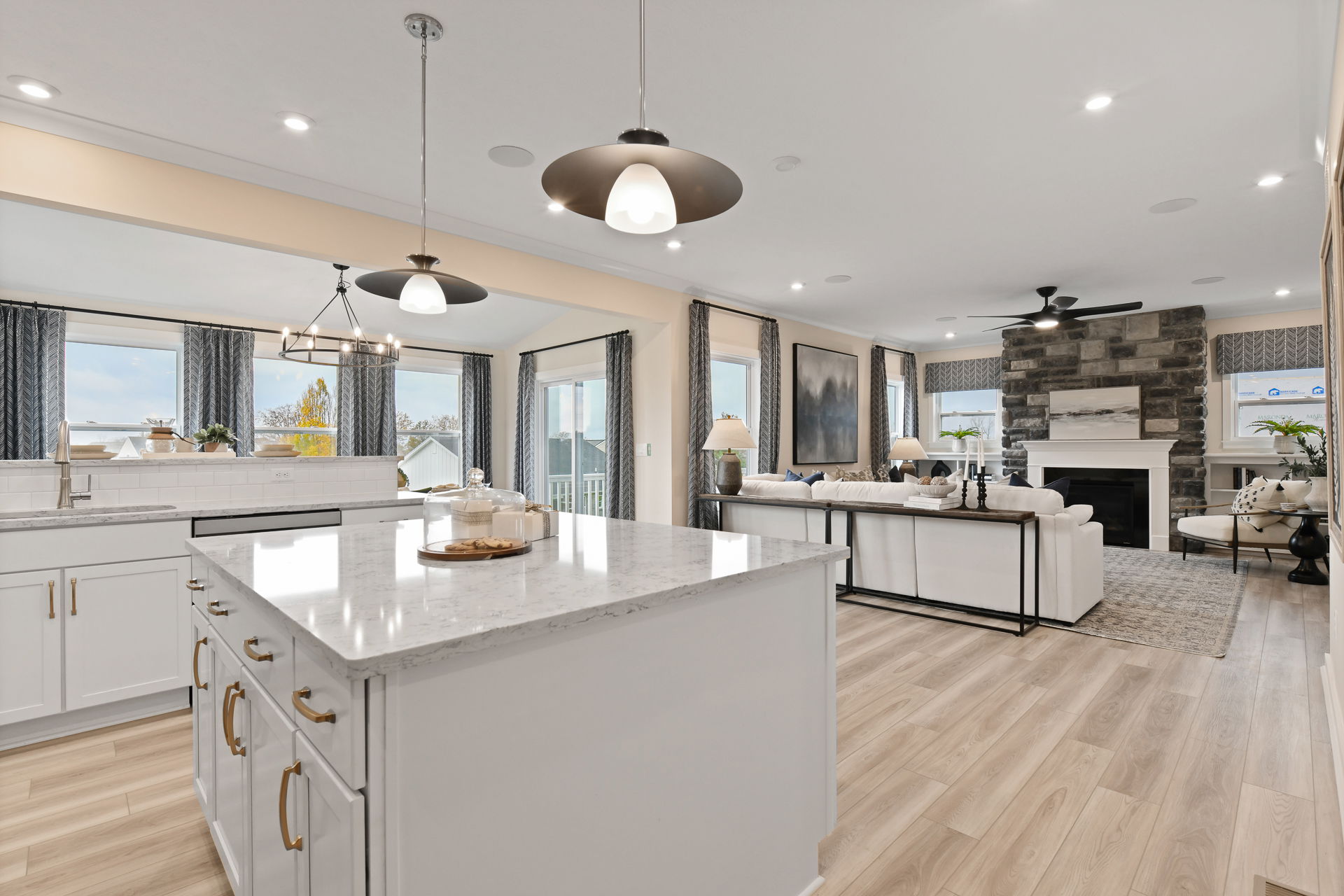 Luxurious open-concept kitchen and living room with modern lighting, stone fireplace, and sleek white cabinetry.