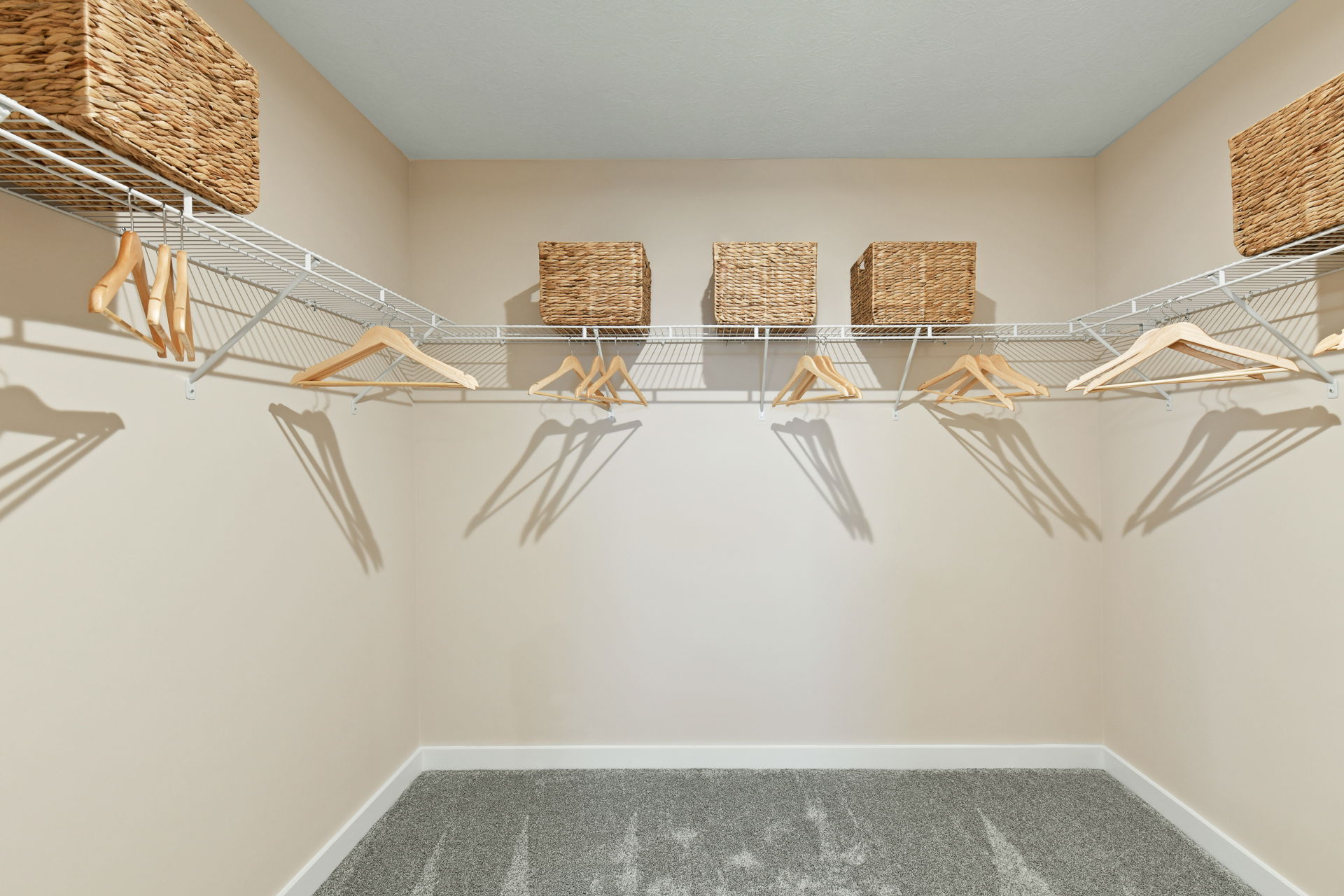 Spacious walk-in closet with empty wooden hangers and wicker storage baskets on wire shelving against beige walls.