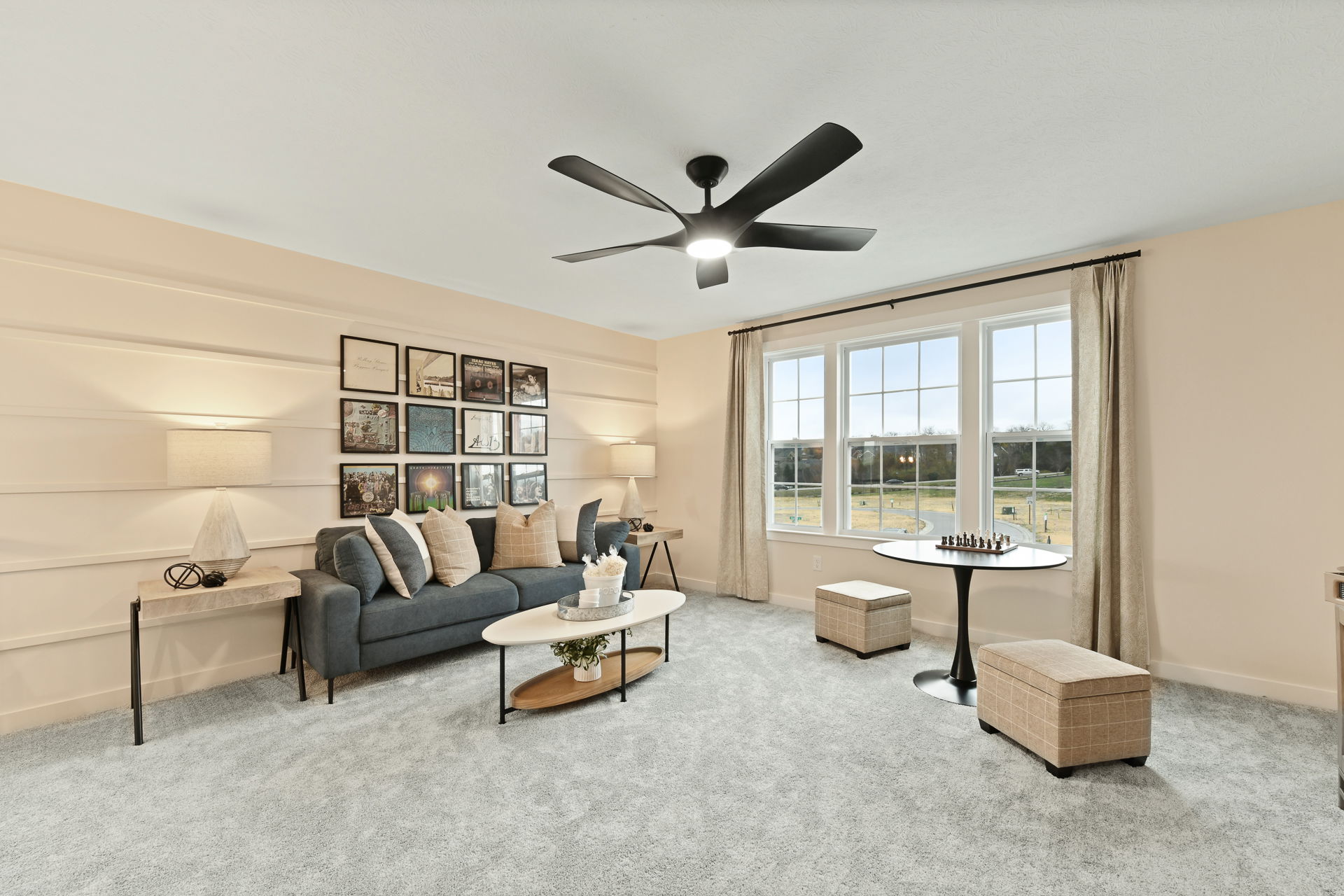 Stylish and cozy living room with contemporary decor, featuring a grey couch with cushions, modern ceiling fan, and large windows offering natural light.