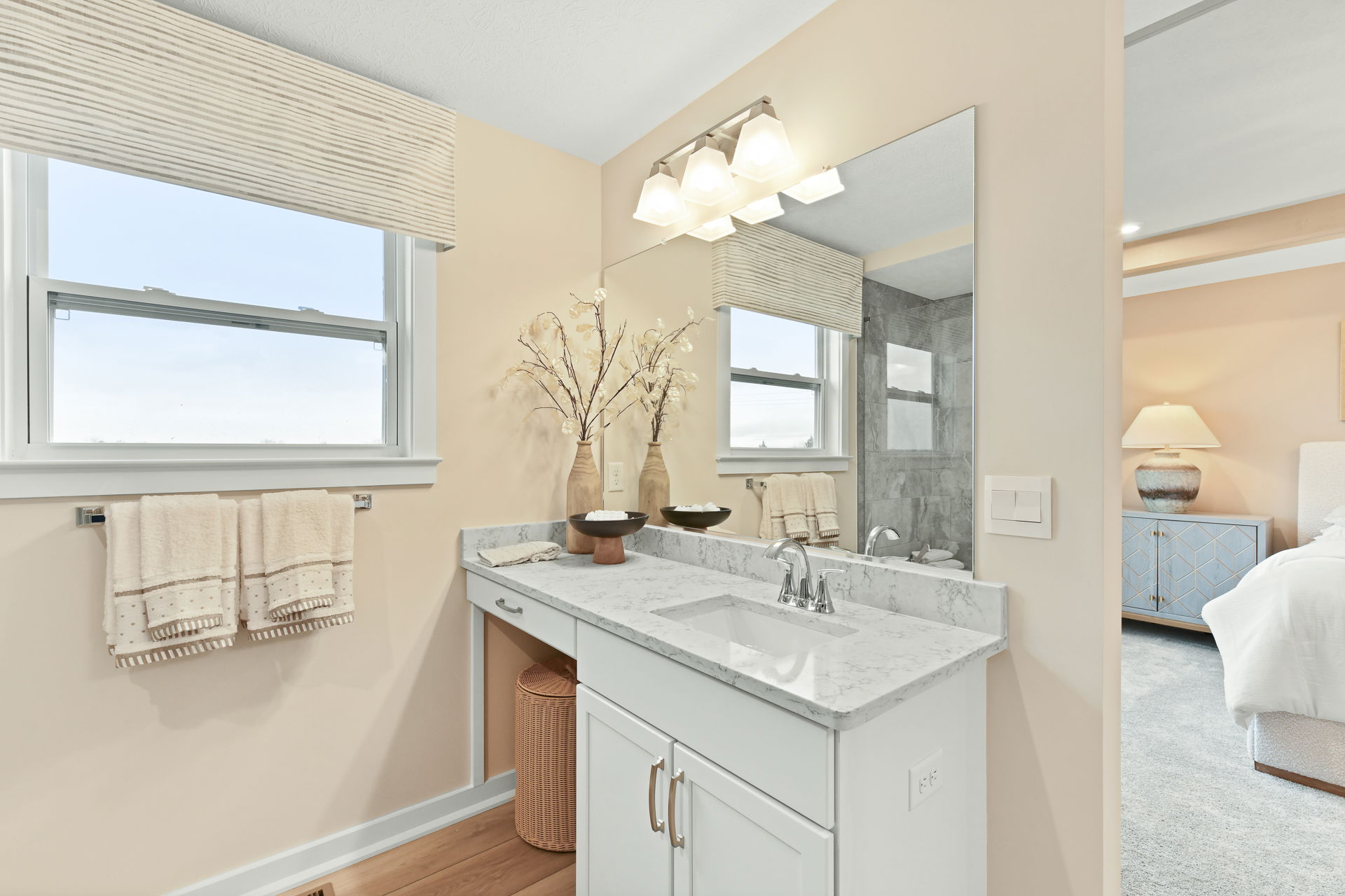 Modern bathroom with a marble countertop, large mirror, and decorative vases beside a bedroom.