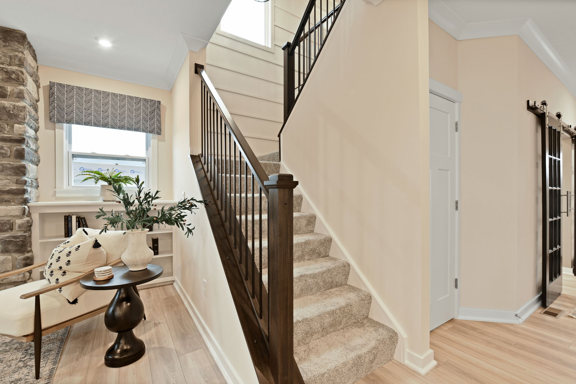 Modern indoor staircase with wooden railing and carpeted steps, next to a cozy sitting area with a table and plant.