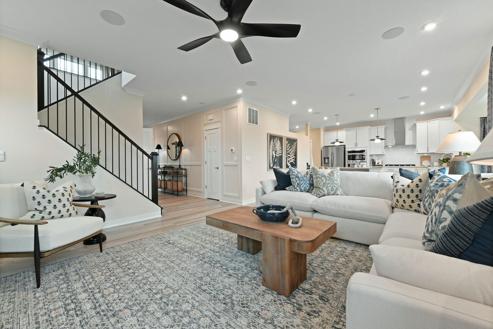 Modern living room with white sectional sofa, wooden coffee table, and open kitchen in a stylish open-concept home.