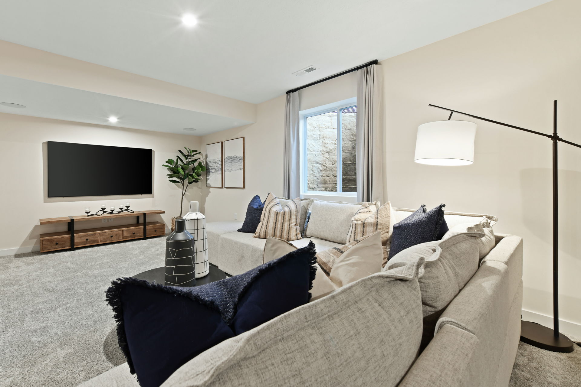 A contemporary living room with a comfortable sectional sofa, modern decor, a large flat-screen TV, and a floor lamp.