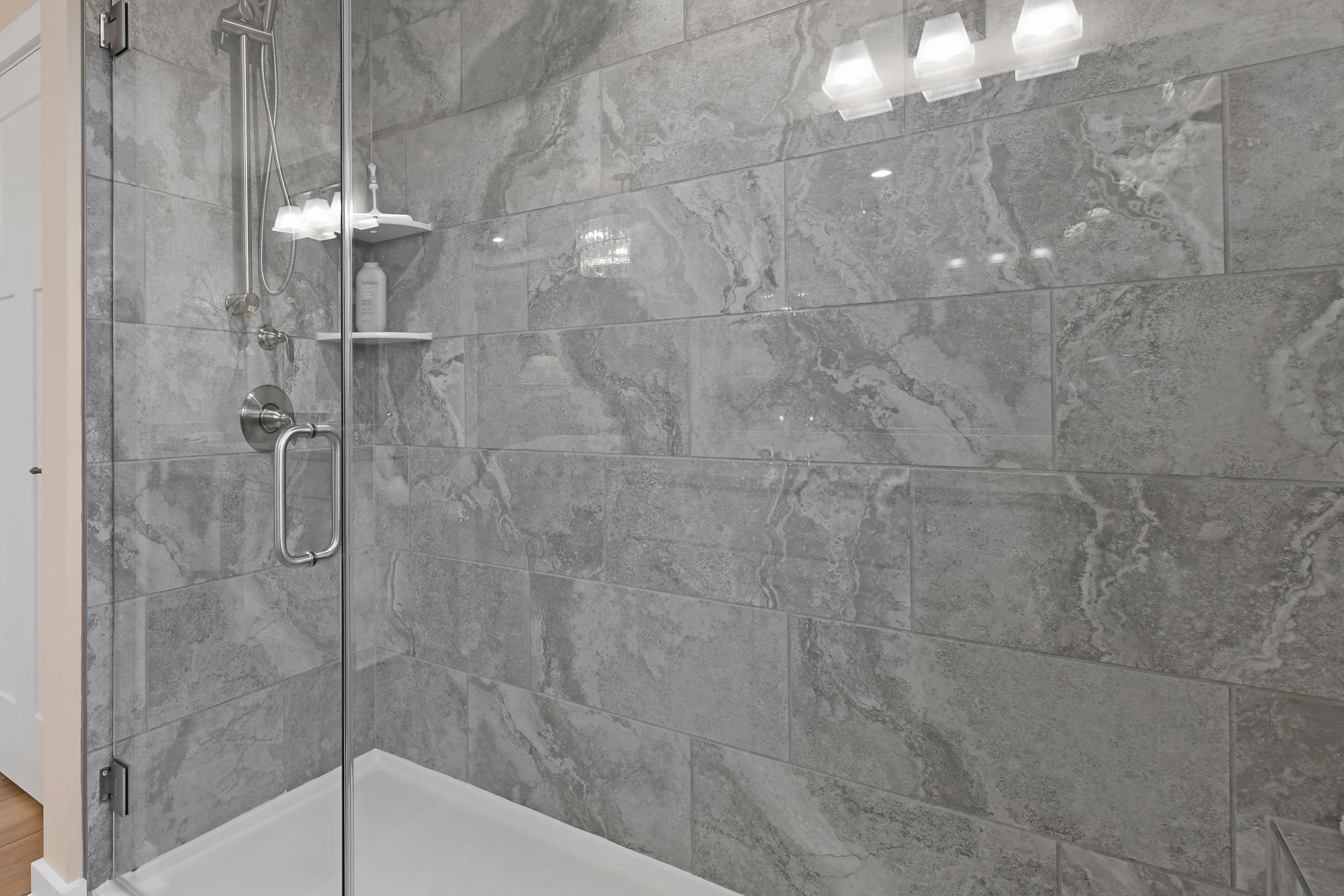 Modern bathroom shower with sleek gray marble tiles, glass door, and chrome fixtures.