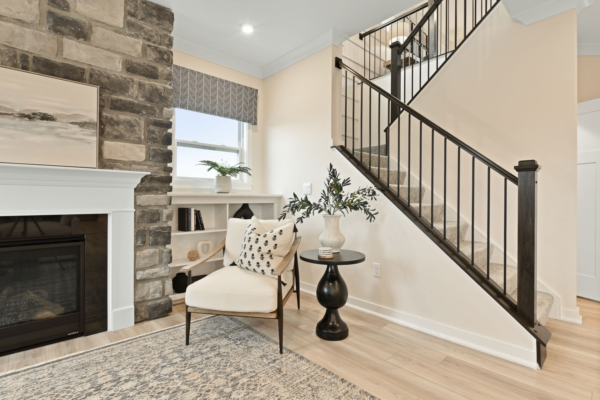 Cozy living room corner with stone fireplace, modern staircase, and elegant armchair in soft, neutral tones.